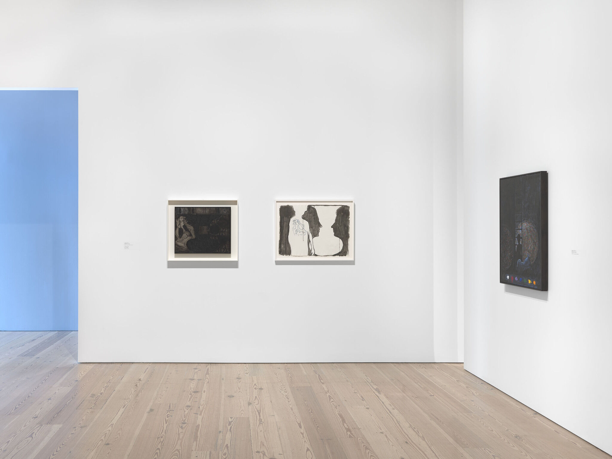A white exhibition wall with three works mounted next to each other. 