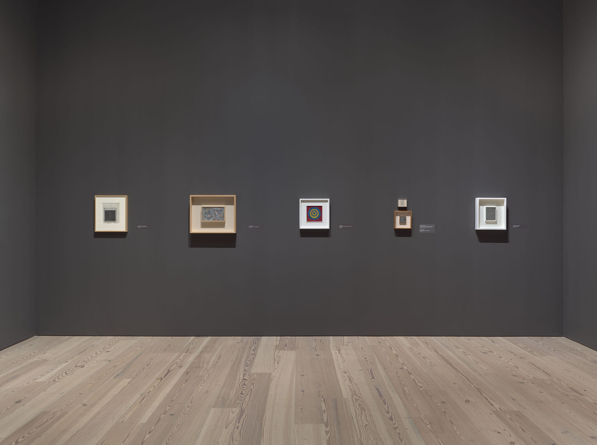 A black exhibition room with framed works mounted on the walls. 