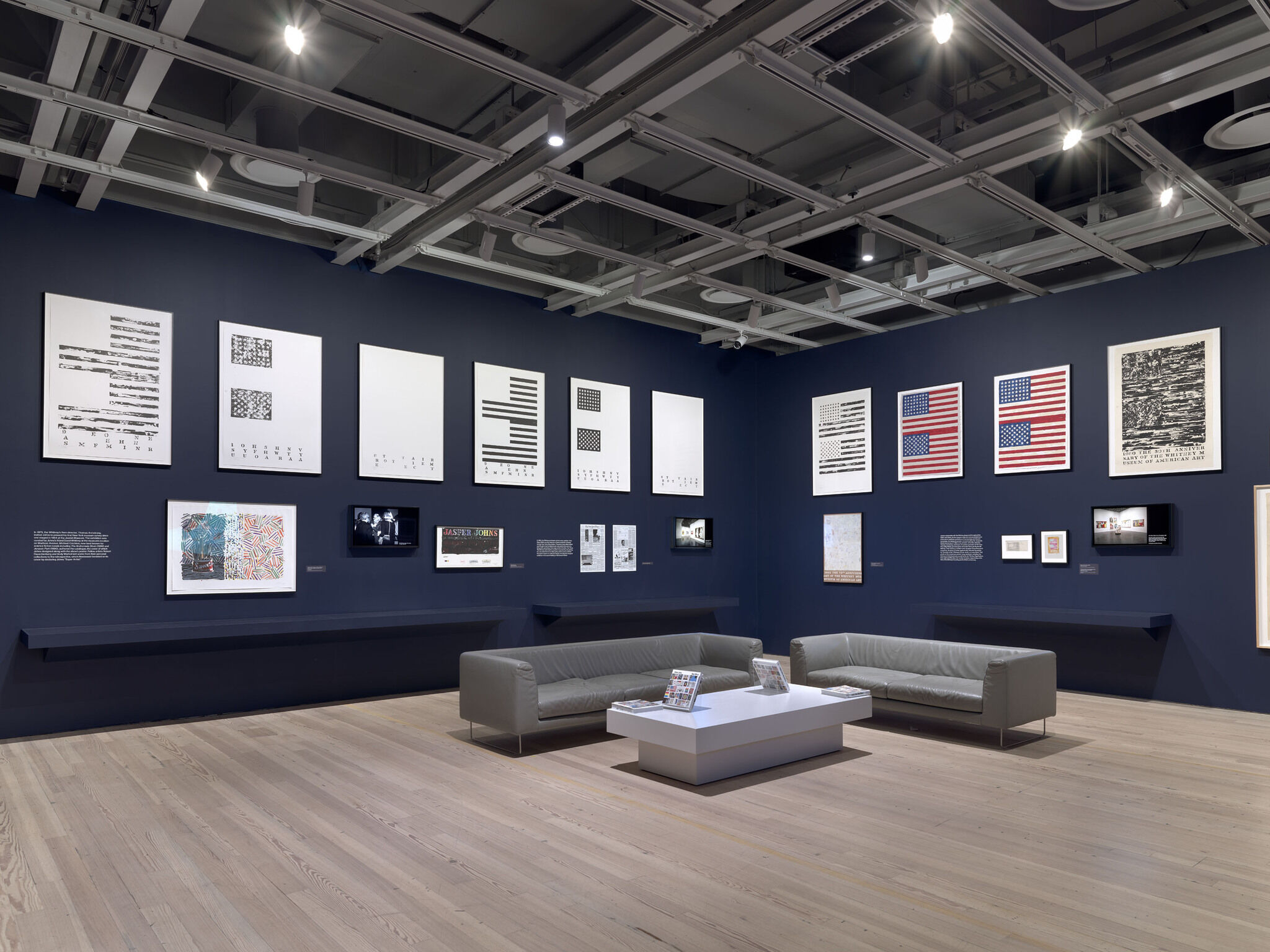 A dark blue exhibition room with a series of printed materials framed on the wall.