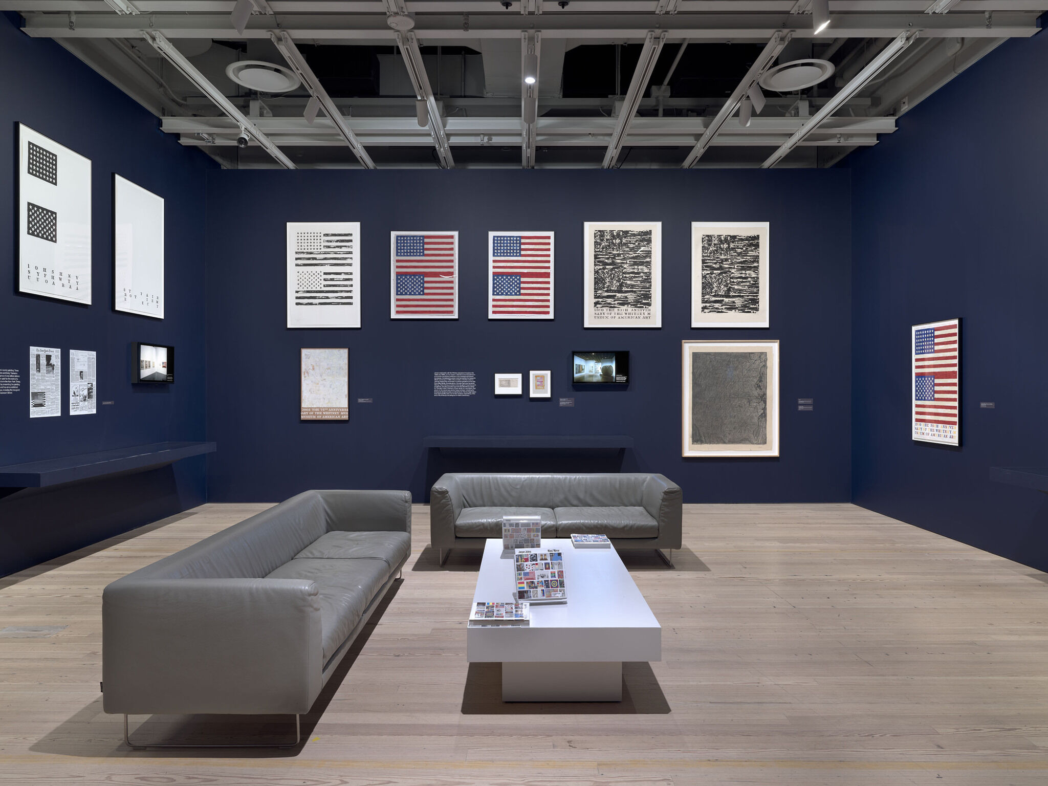 A dark blue exhibition room with a series of printed materials framed on the walls.
