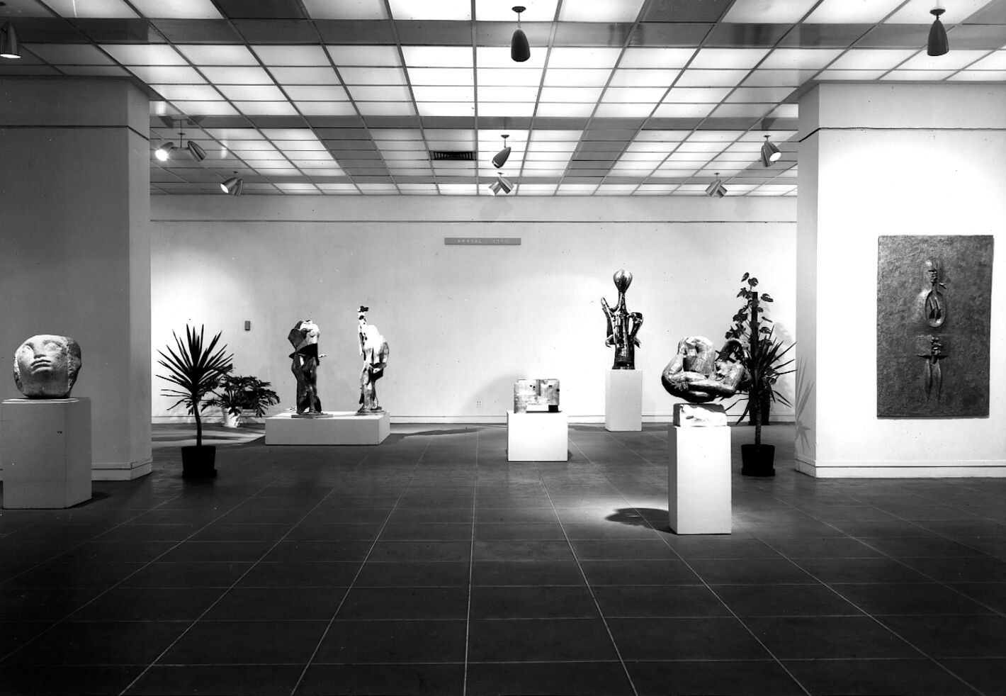 Black-and-white photograph of a gallery filled with works of art.