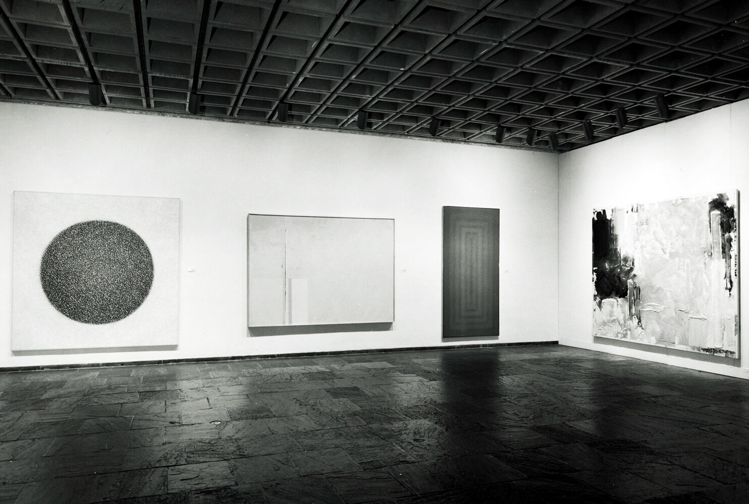 Black-and-white photograph of works of art hanging in a gallery.