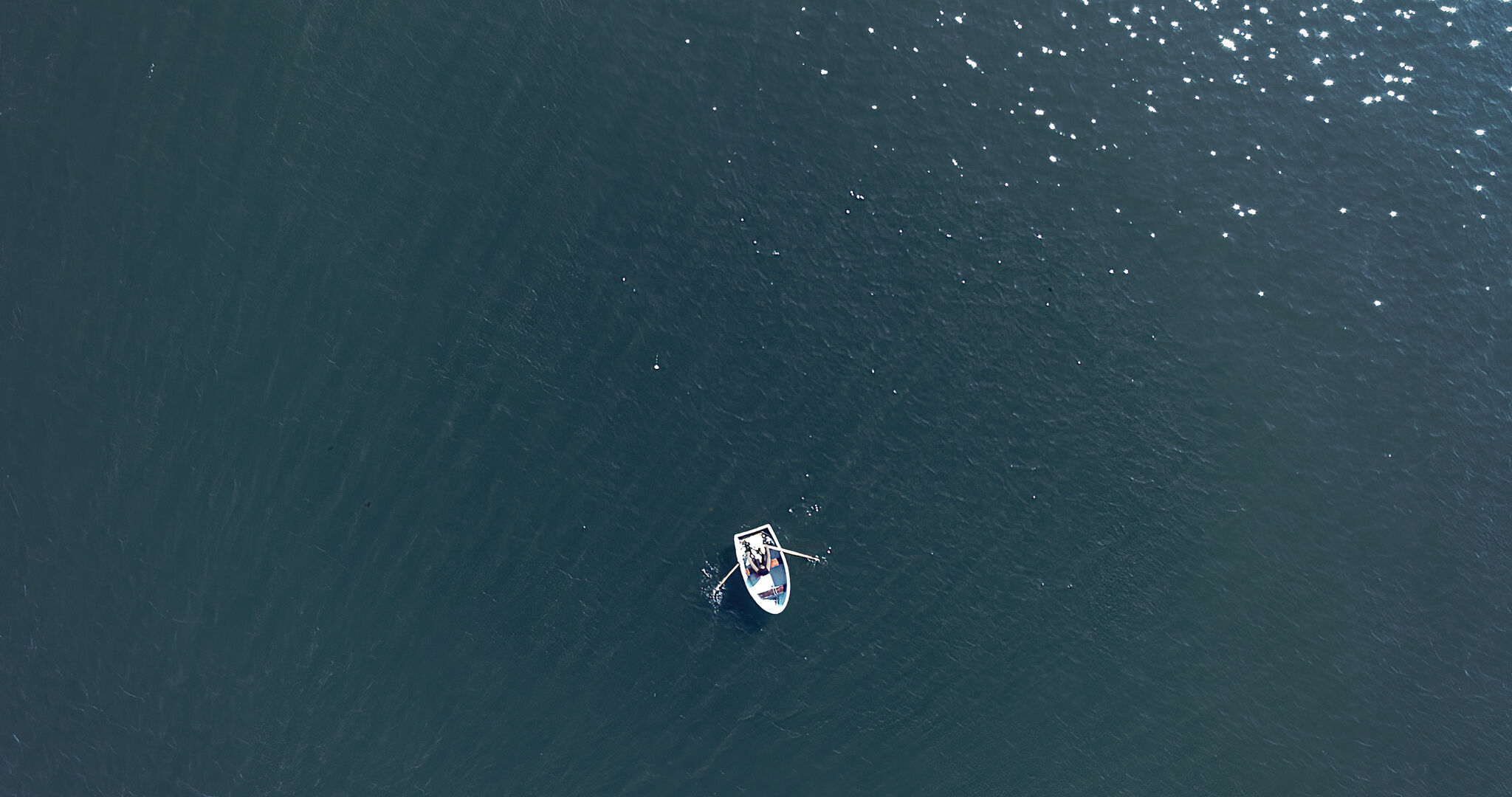 A small, white rowboat in the middle of an expansive, gray-blue body of water.
