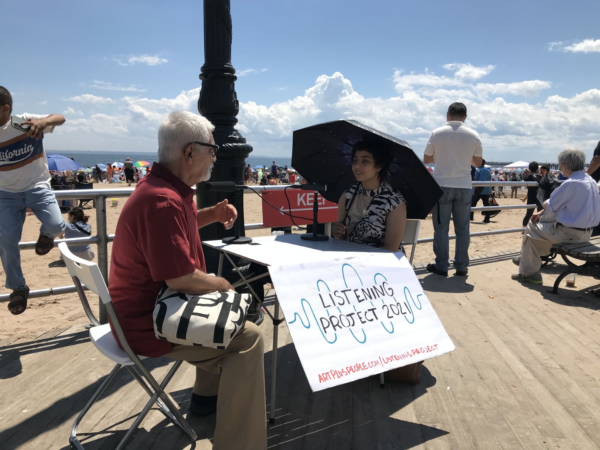Two people sitting on a boardwalk talking into microphones. 