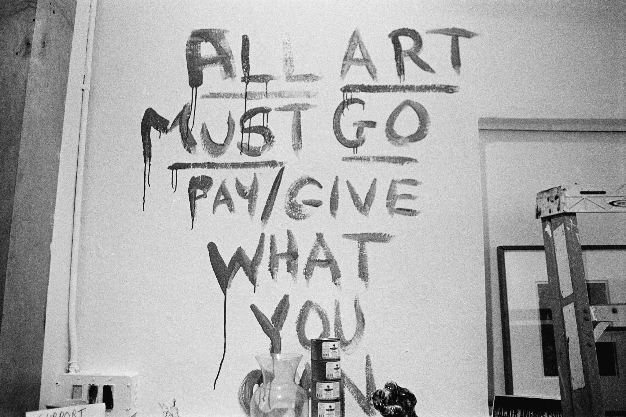 A wall painted with the phrase All Art Must Go. Pay/Give What You Can. 