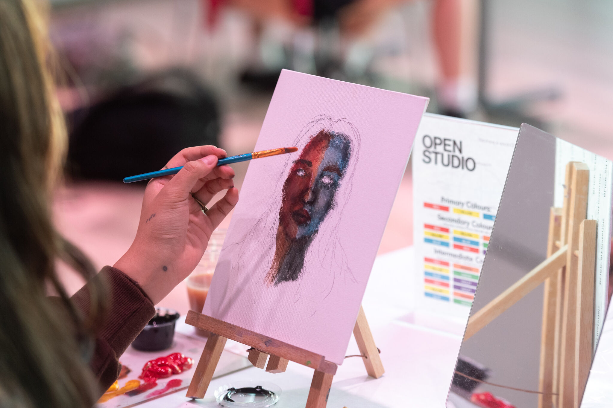 A close-up of a person's hand painting on a small canvas. 