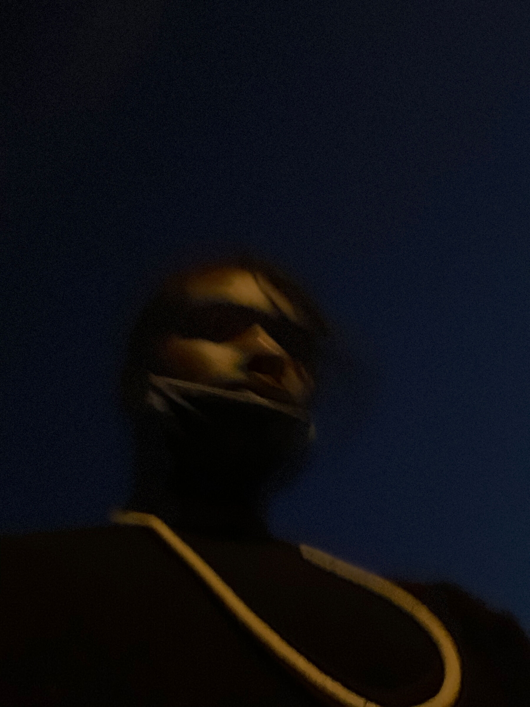 Blurry image of a person seen from a low angle, dressed in dark clothing and set against a dark blue background.
