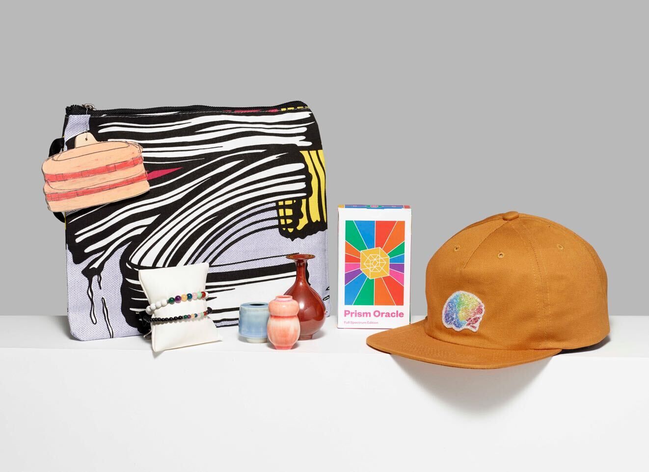 A stationary pouch, burnt-orange hat, and a series of other items from the Whitney shop displayed on a white surface.