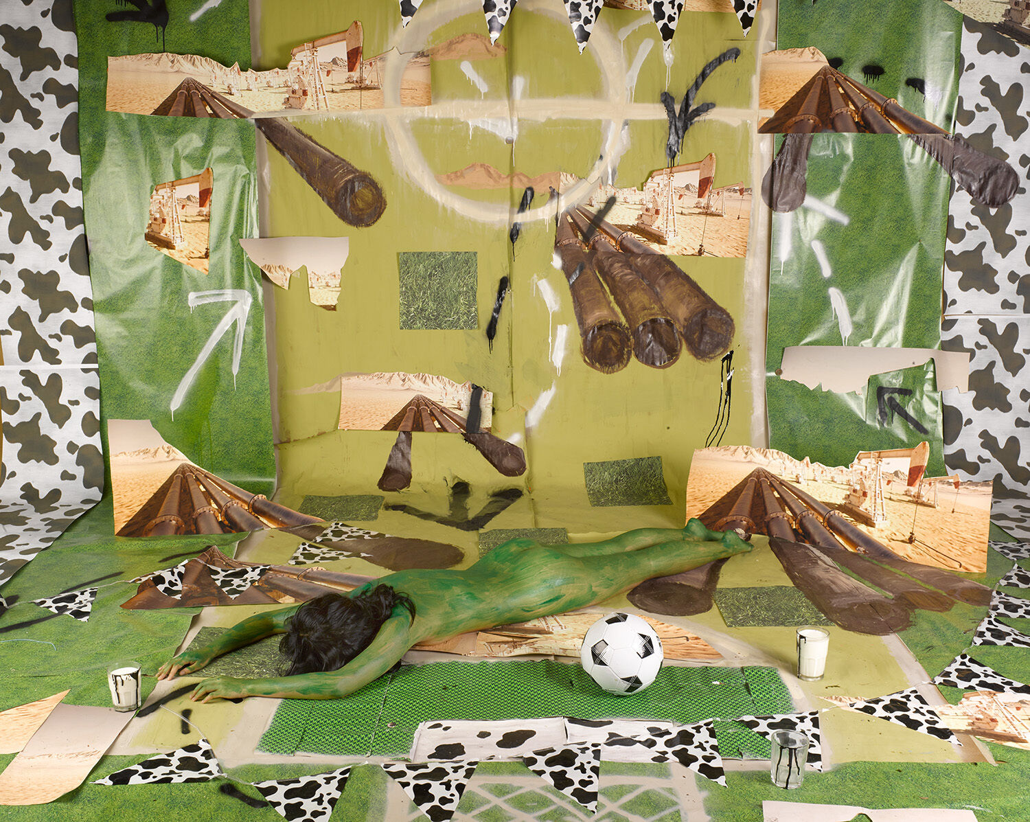 A person painted in green lays face down against a collaged background.