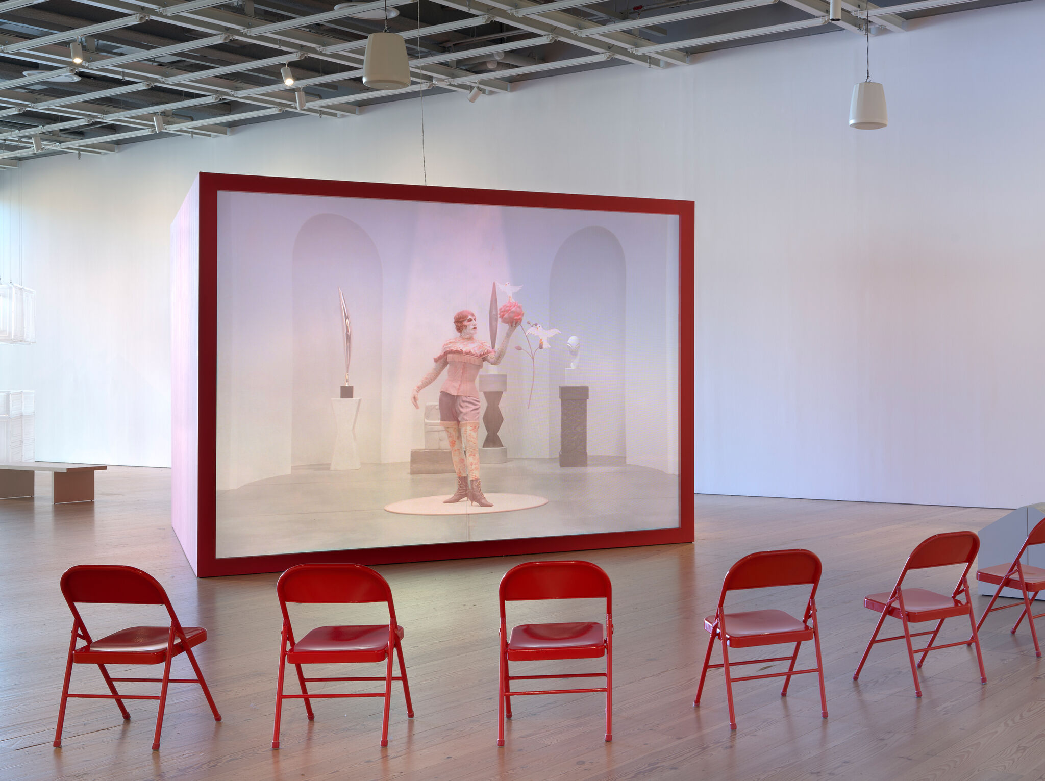 Image of a sculpture gallery projected against a large, red cube.