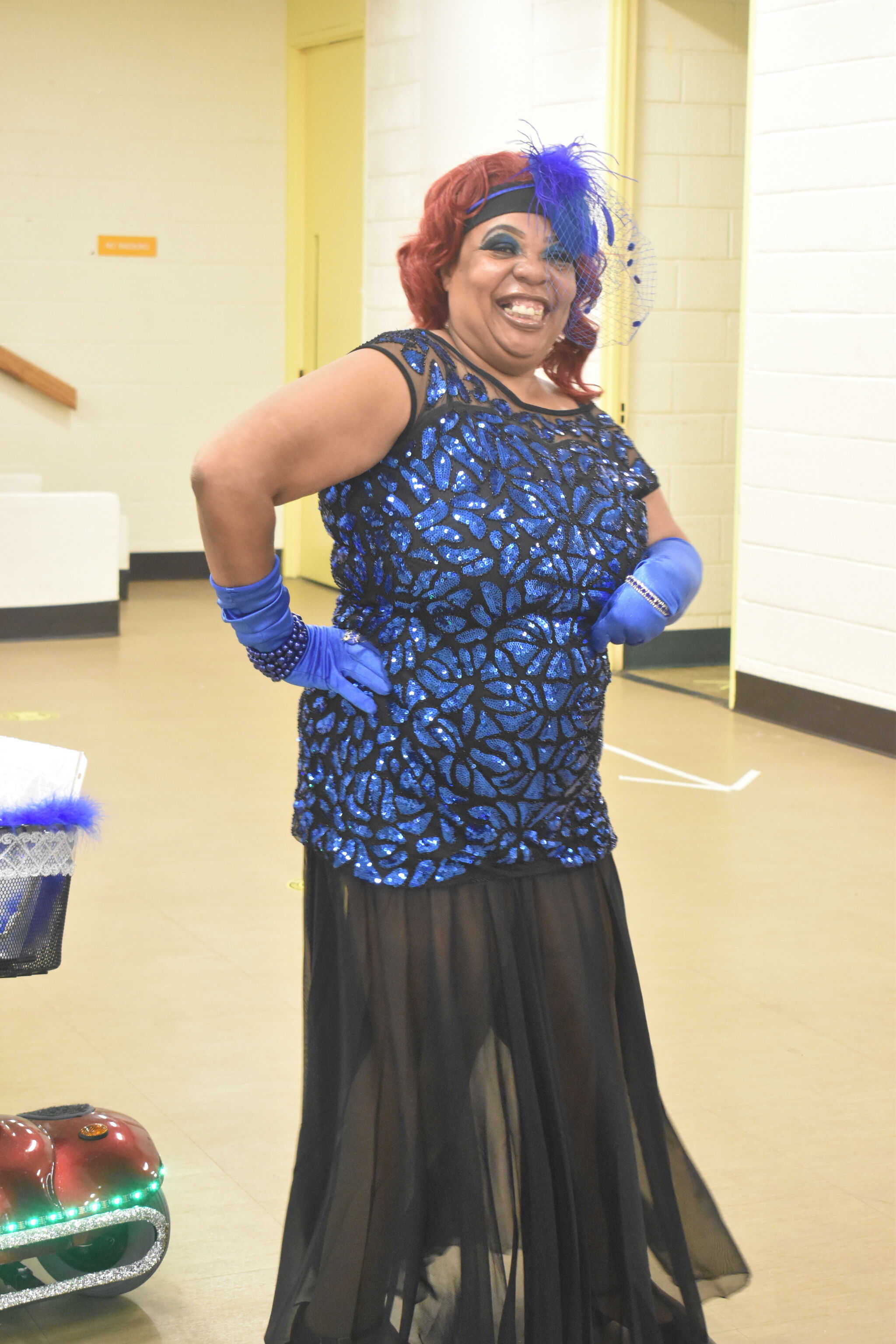 A person dressed in a blue gown and blue gloves, looking at the camera and smiling. 