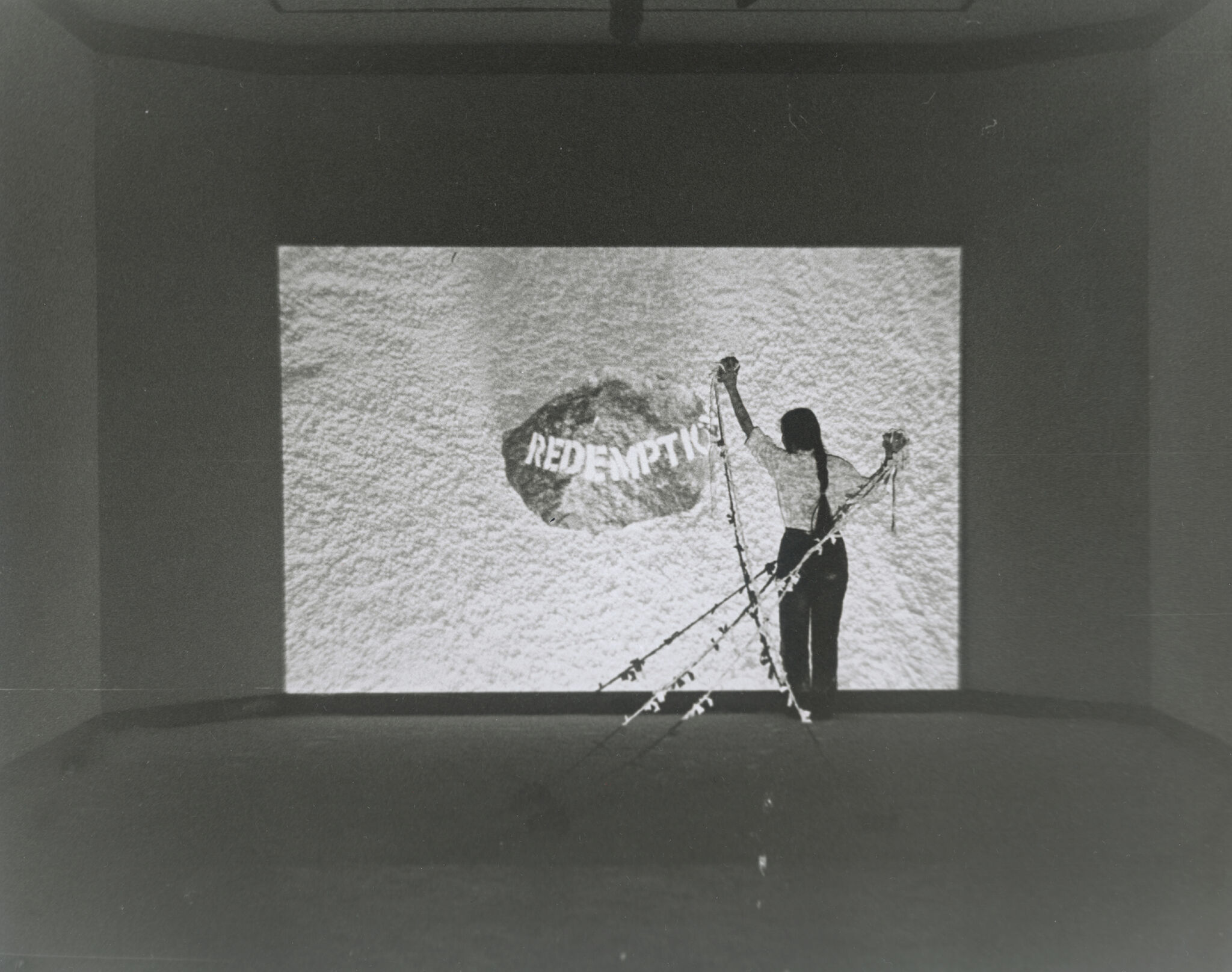 A grayscale image of a person standing in front of a projected screen. 