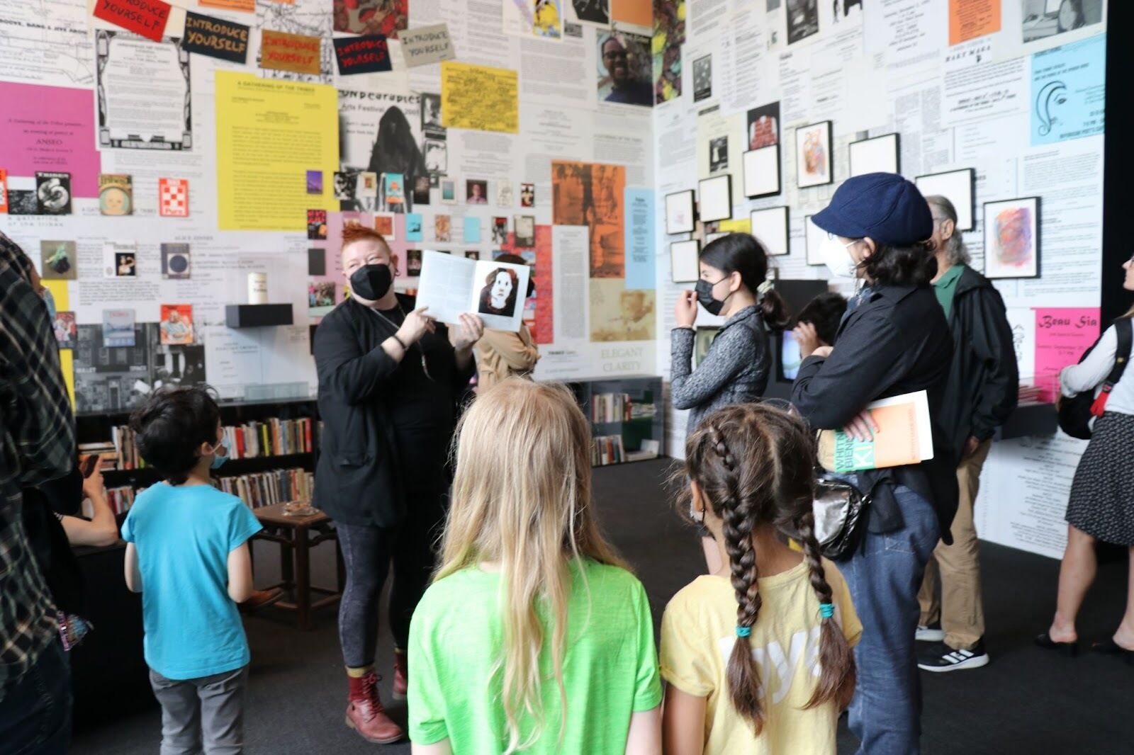 A small crowd of people surround poet Chavisa Woods as she holds a pamphlet and presents to them for a family tour. 