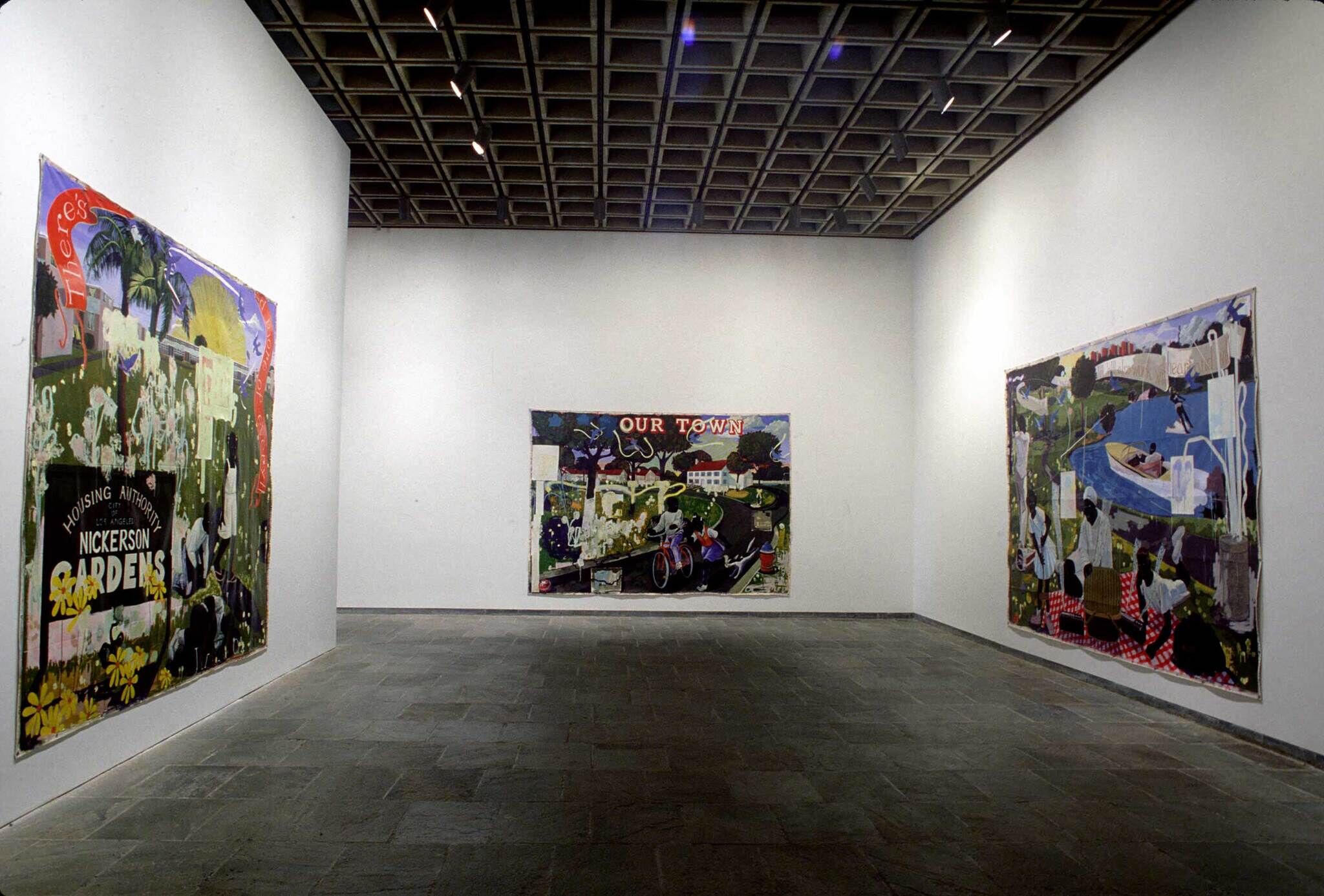 Art gallery with three colorful paintings on white walls, featuring urban and rural scenes. Dim lighting and a tiled ceiling.