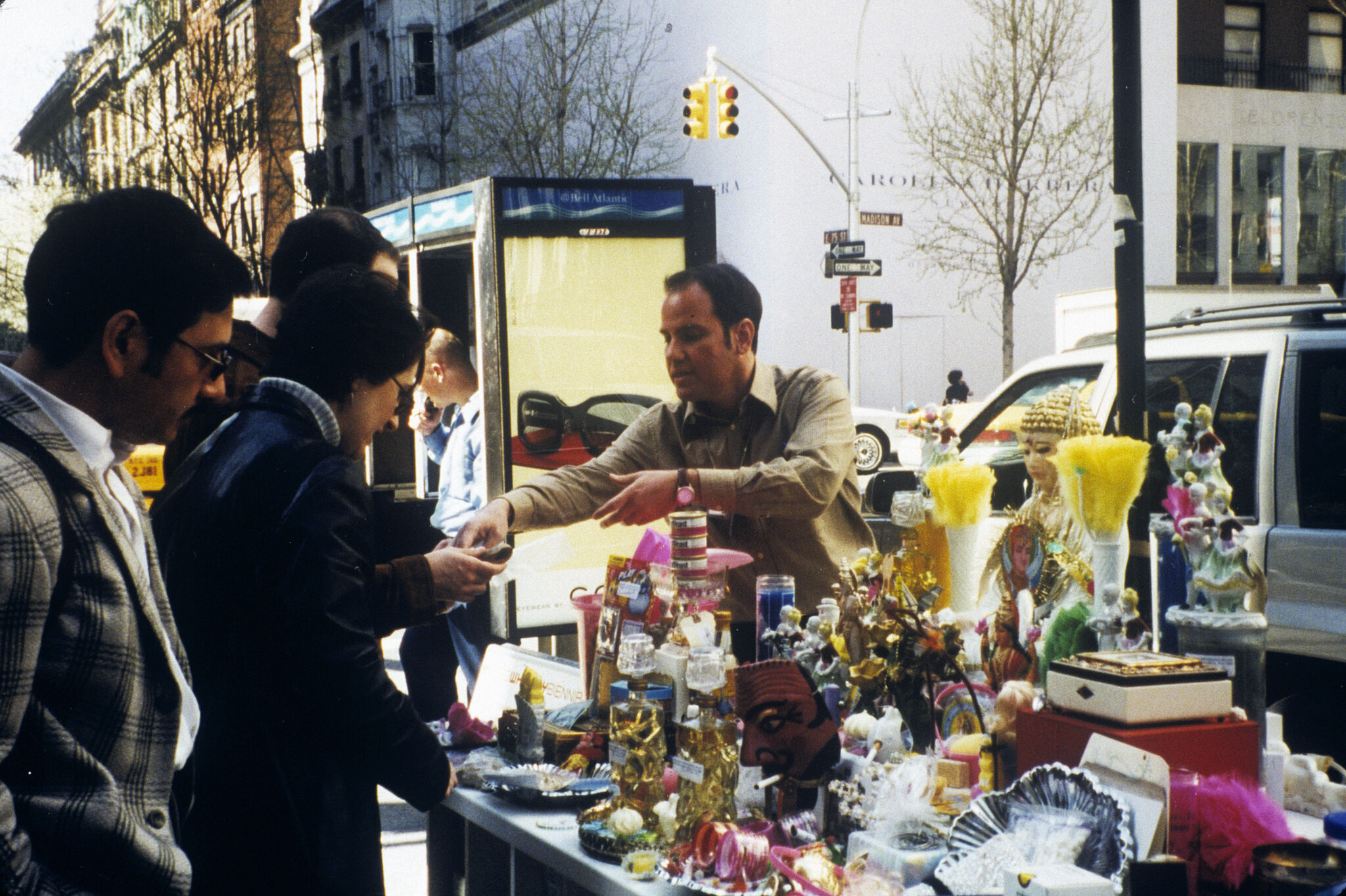 A salesman attending to customers over a table of miscellaneous objects on a New York City street.