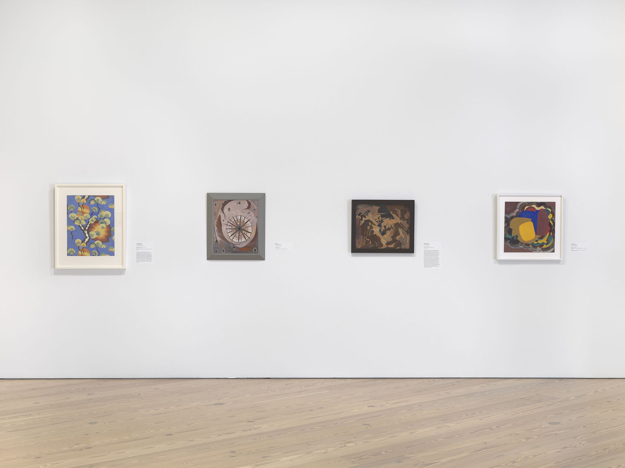 A white exhibition wall with four works installed across it.