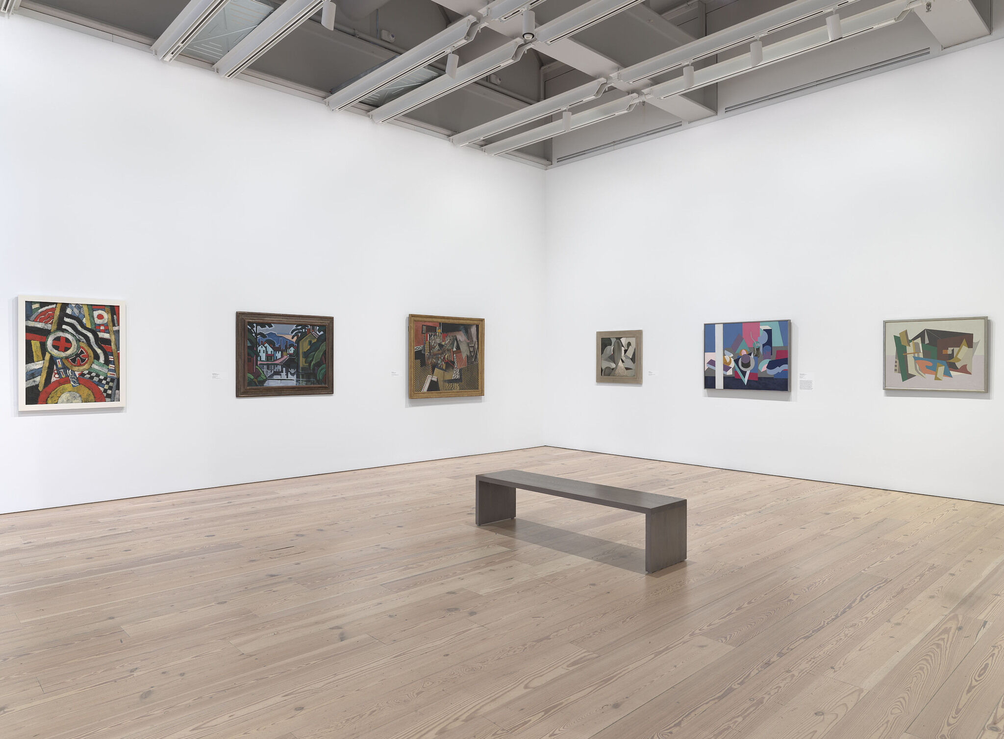 A white exhibition room with six works mounted across two walls. 