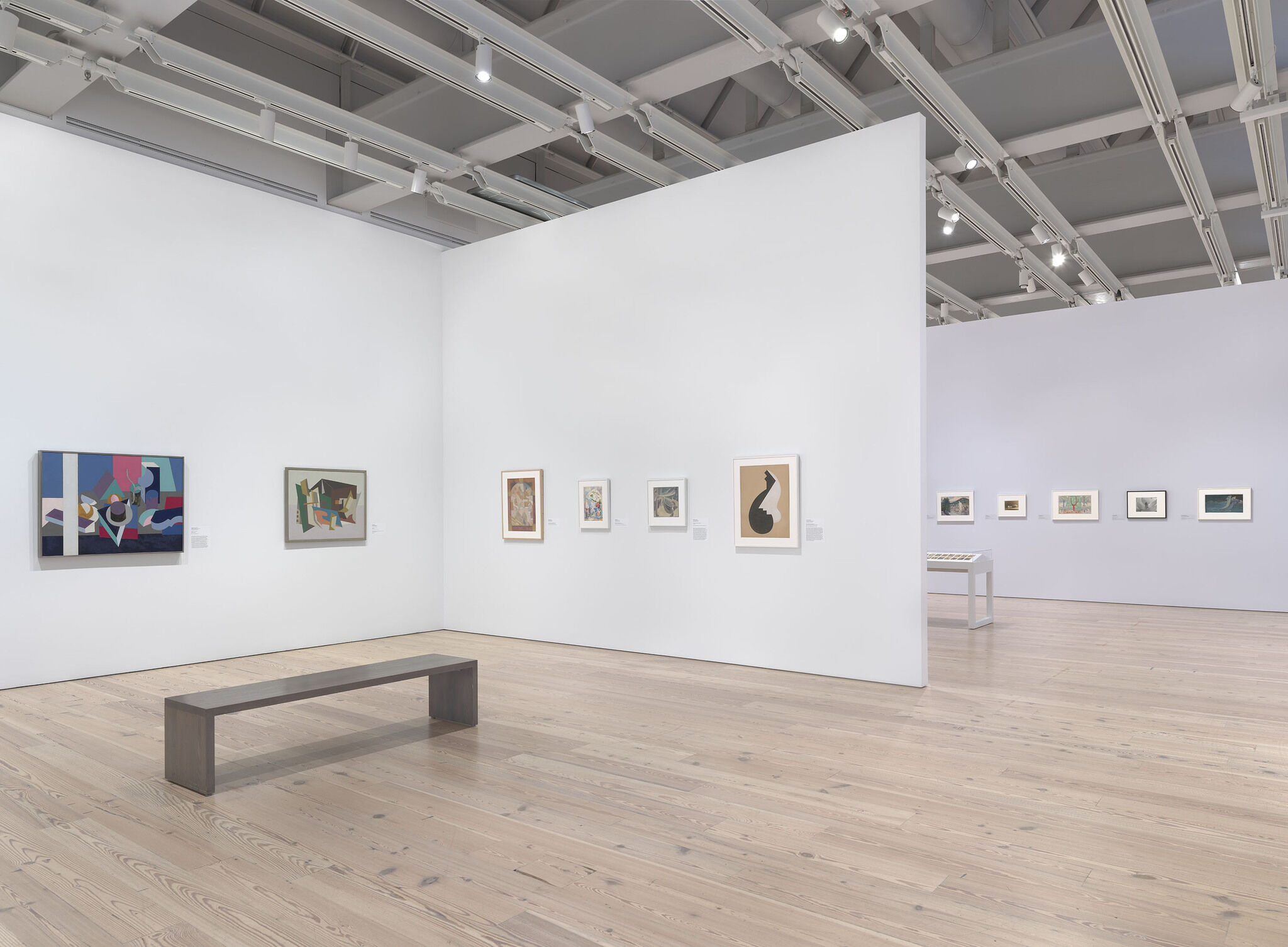 A white exhibition room with eleven works mounted across three walls. 