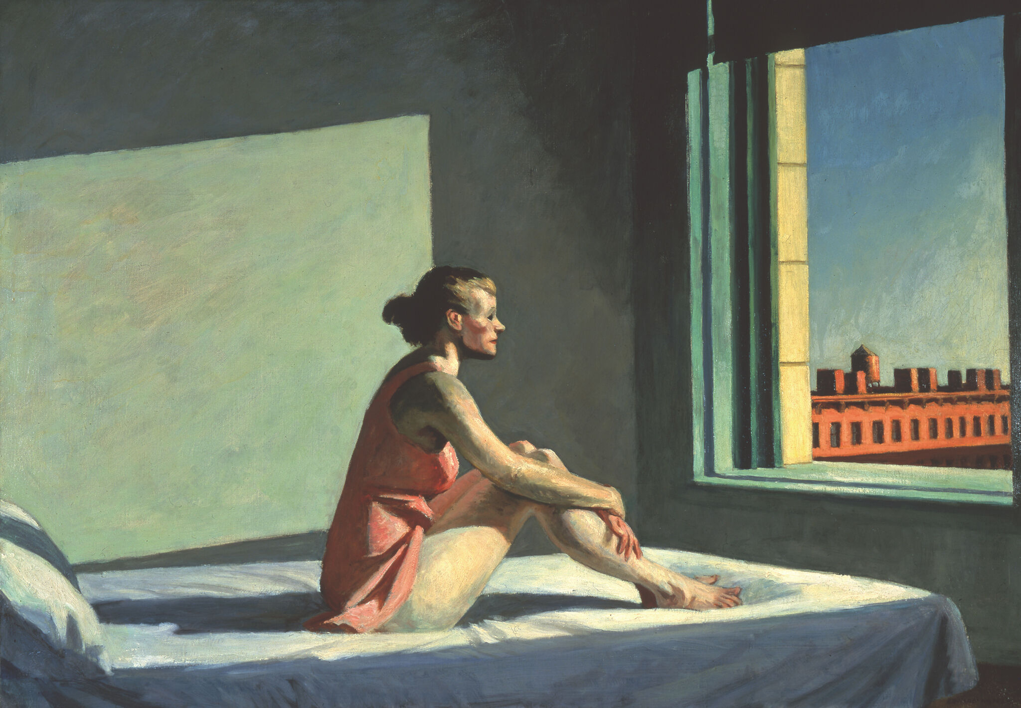 Woman seated on bed looking out window to city view.