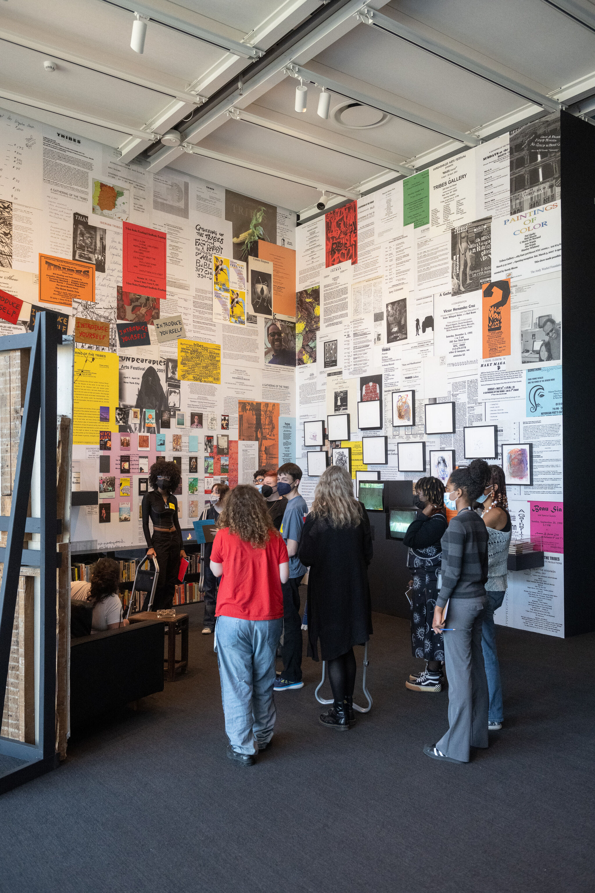 A group of teen visitors stand in front of an installation comprised of two walls collaged with various paper materials and pieces.