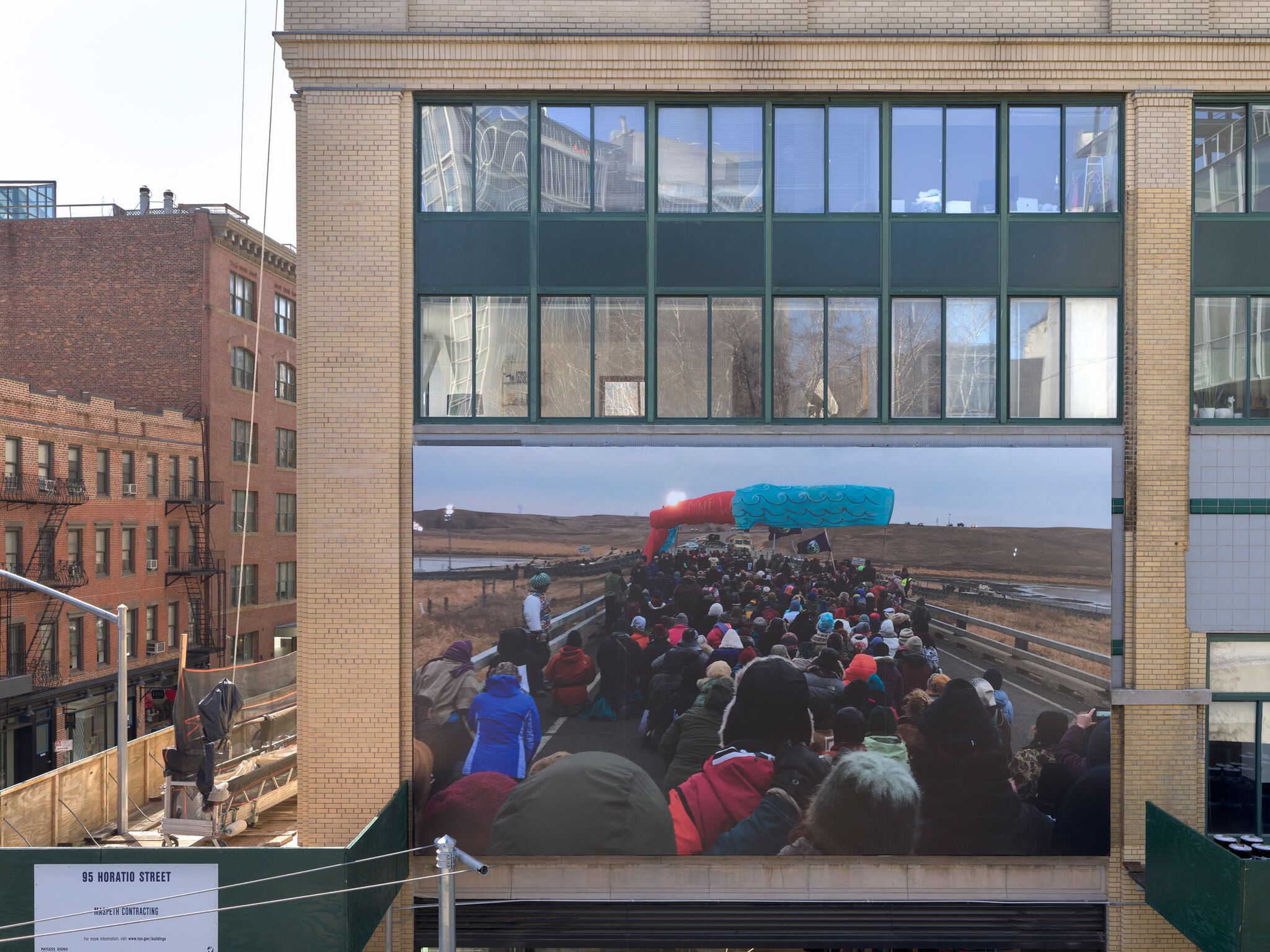 A photograph of a crowd of people is an outdoor billboard. 