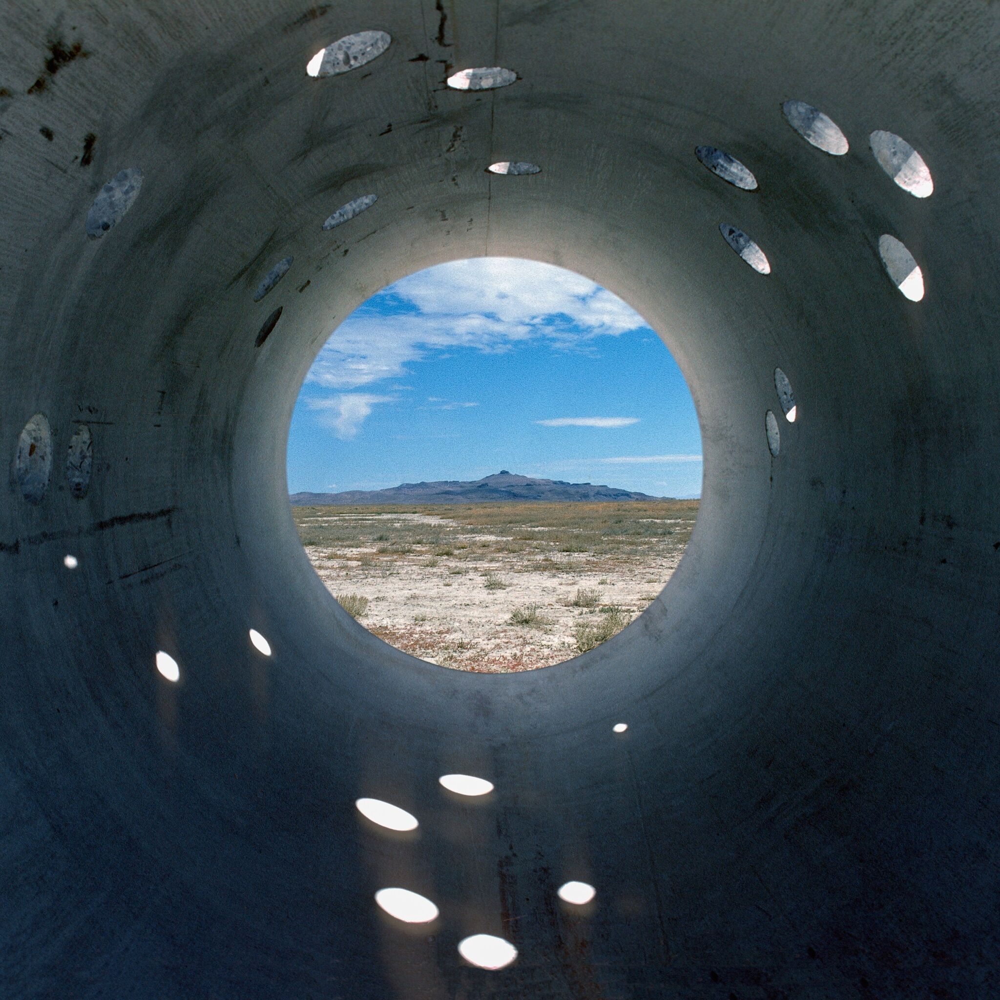 A photograph from inside a large steel tube with a direct view of mountains in the distance.
