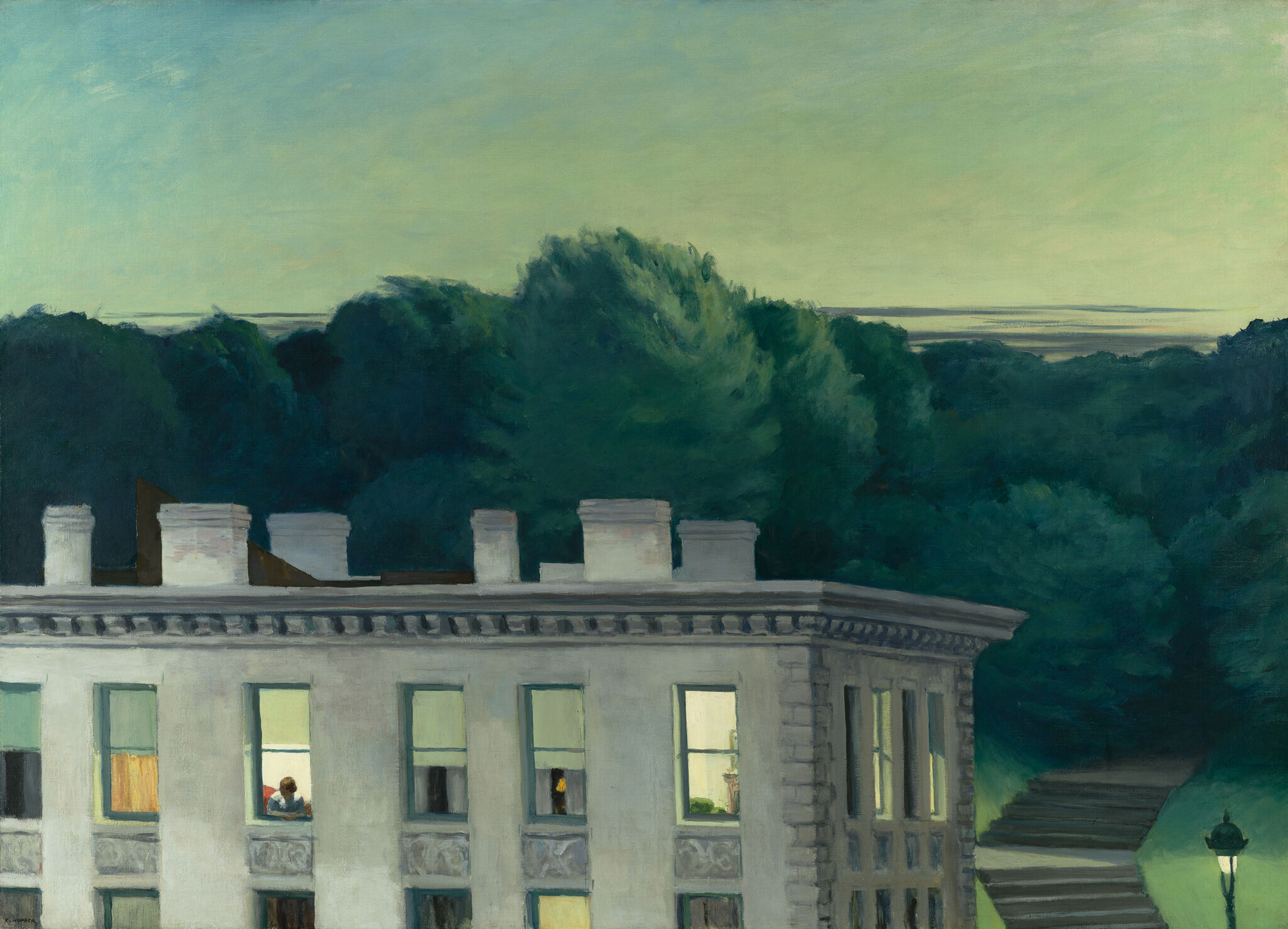 A glowing sky behind the top of a white building and trees.