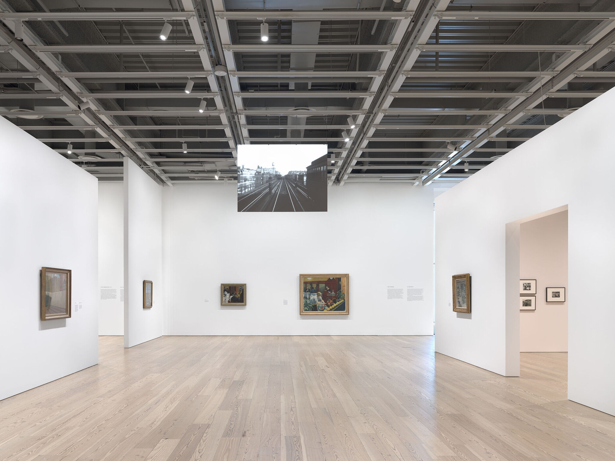 Three gallery walls with artworks hung up and a video projected on a screen. 