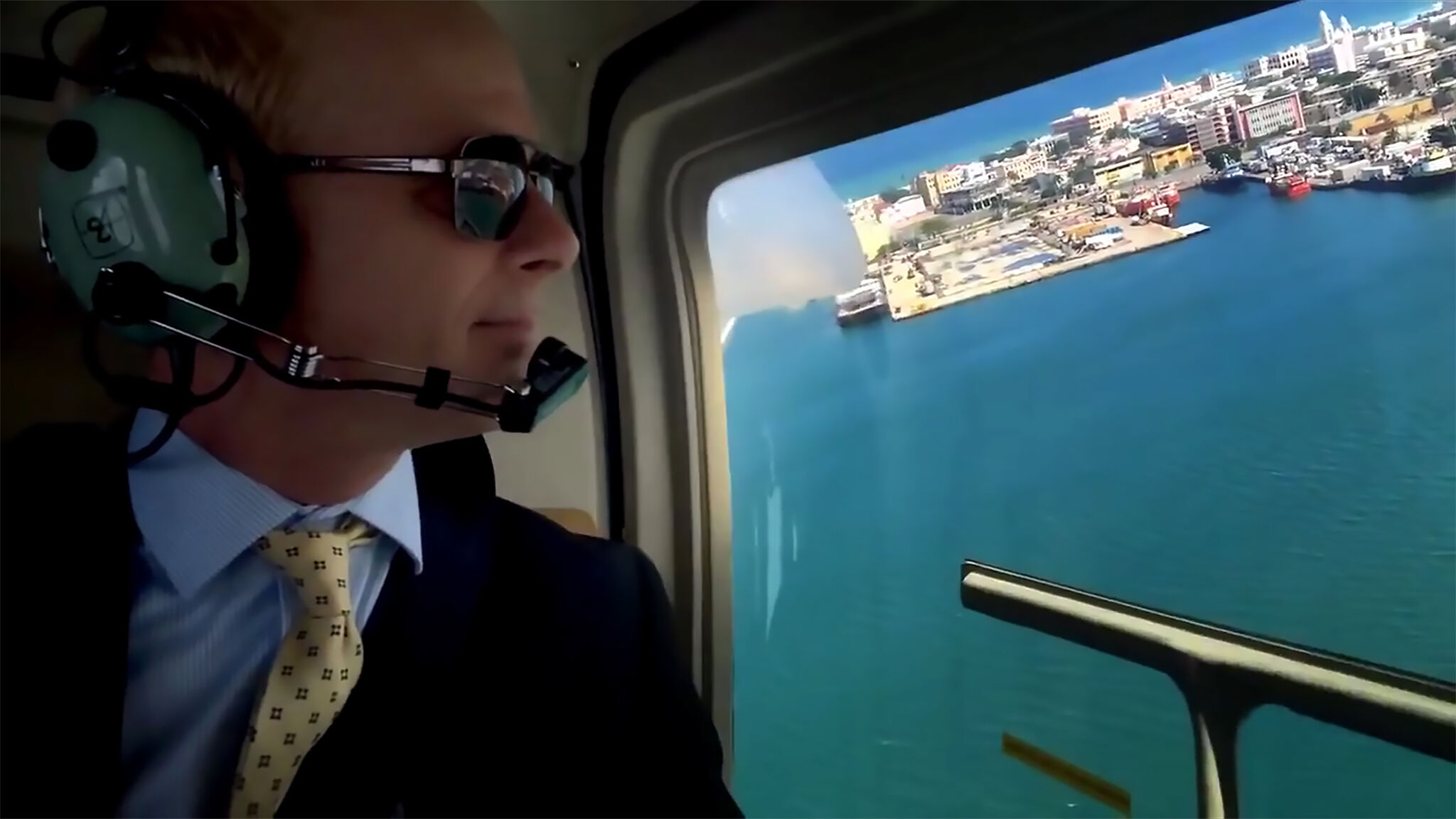 Man in a suit peering out the window of a helicopter. 