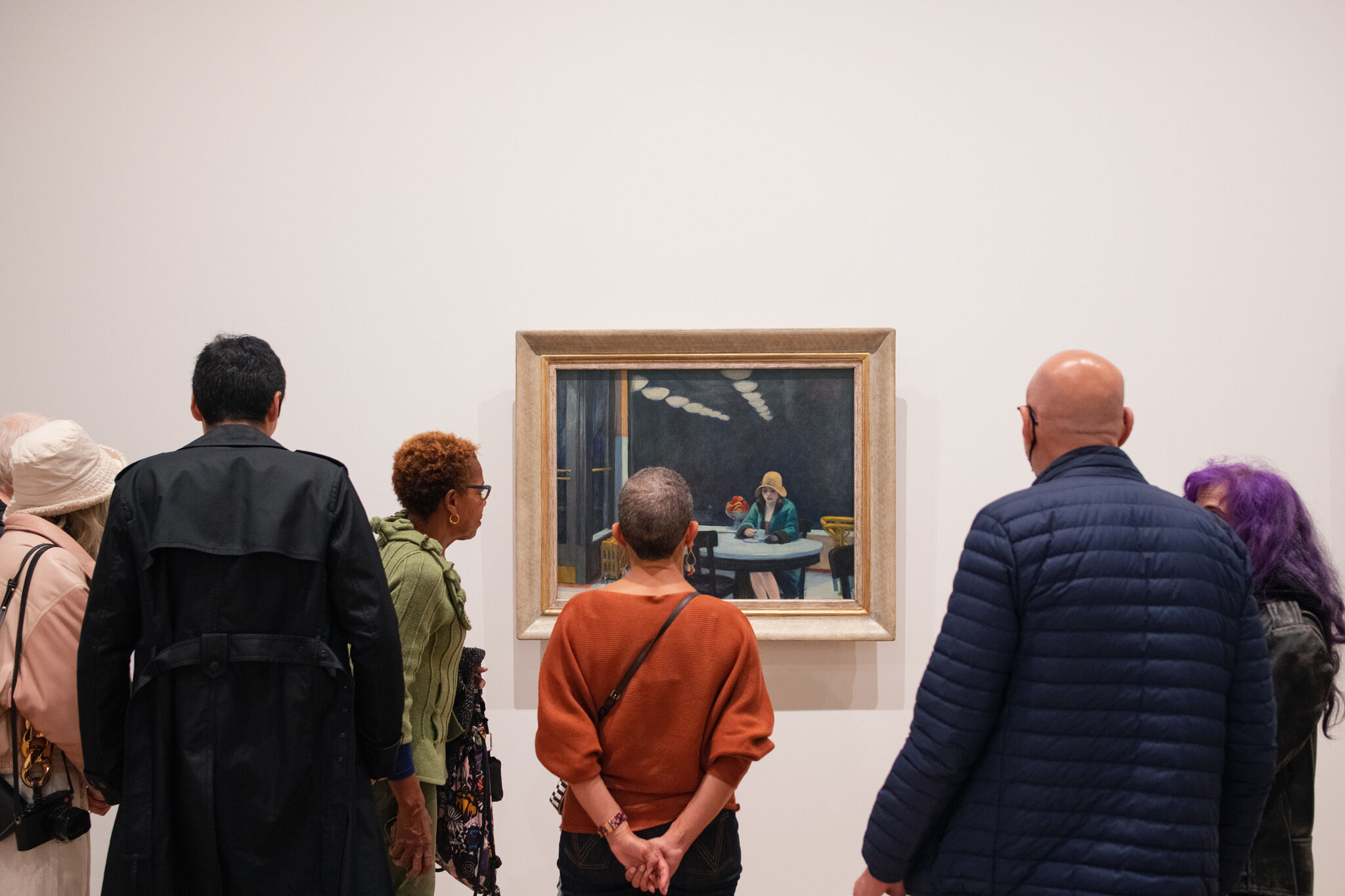 A group of people stands around a painting by Edward Hopper.