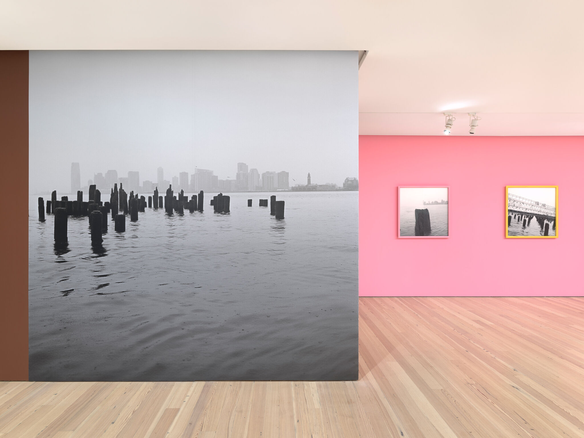 Black and white image of the Hudson River taking up a full gallery wall, next to a pink wall with two balck and white images.