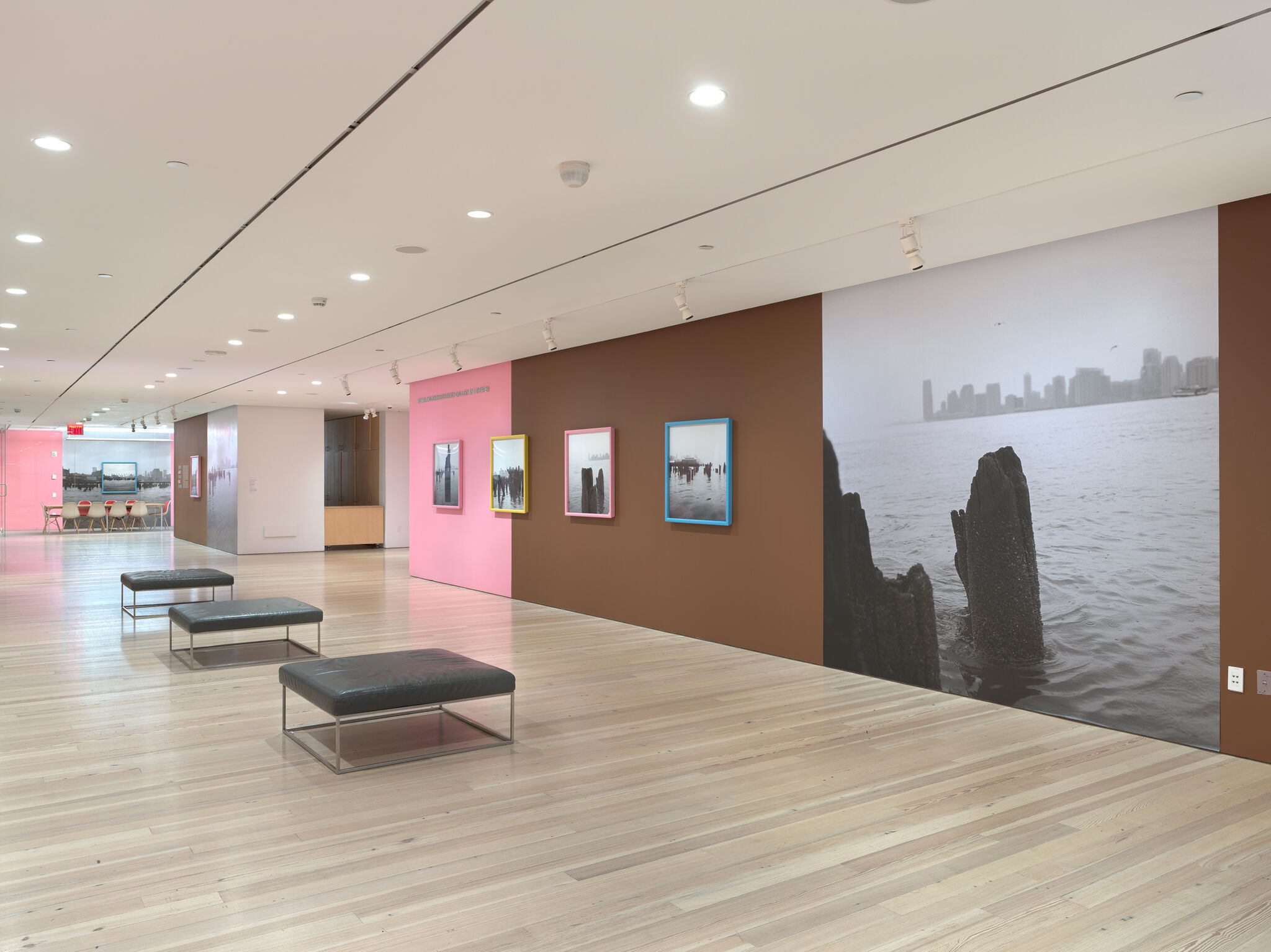 Four black and white photographs of Manhattan's westside waterfront on a pink and black gallery wall next to a large photograph of the Hudson River.