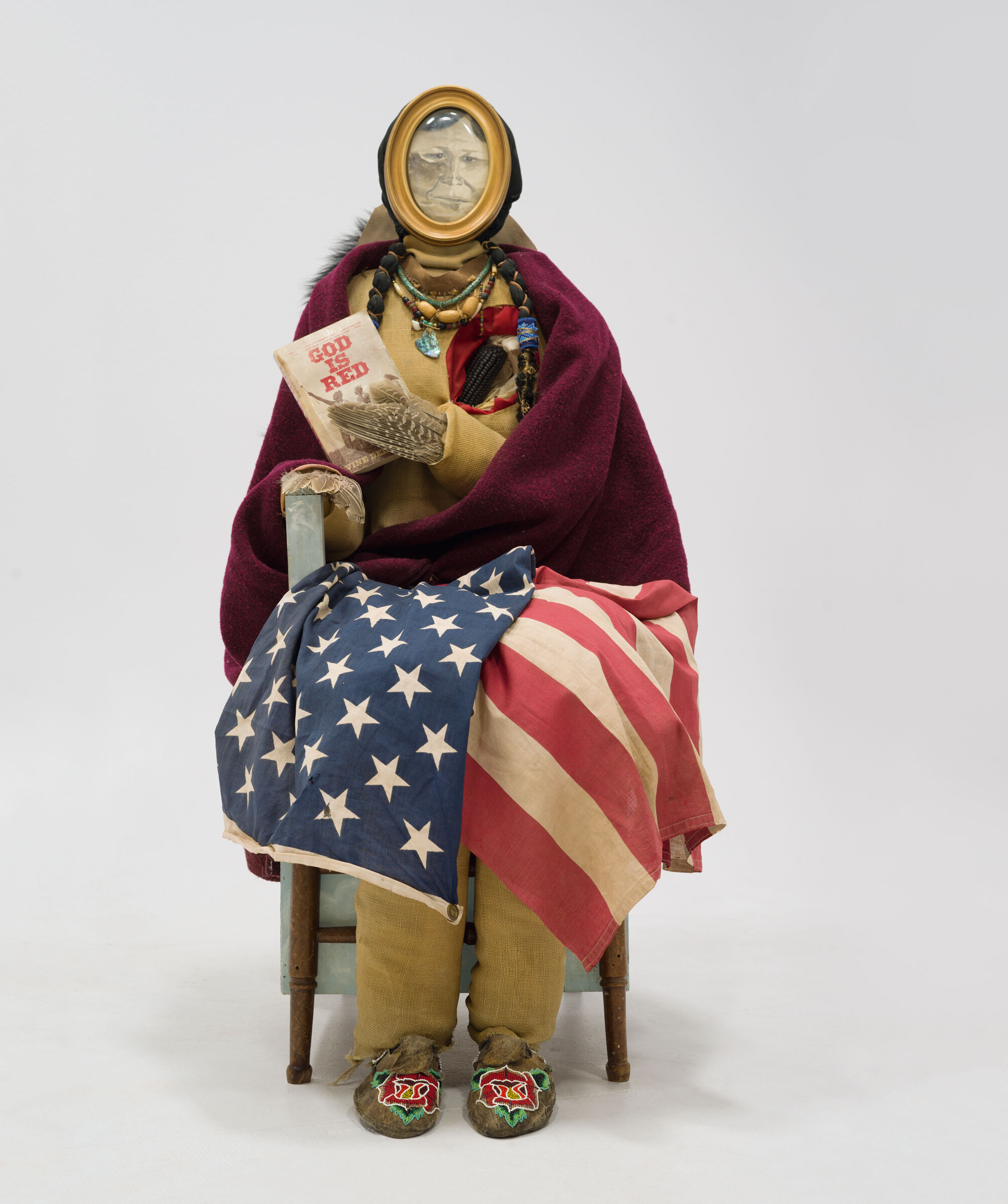 A human with a sketch as a face covered in a flag and holding a book titled "God is Red."