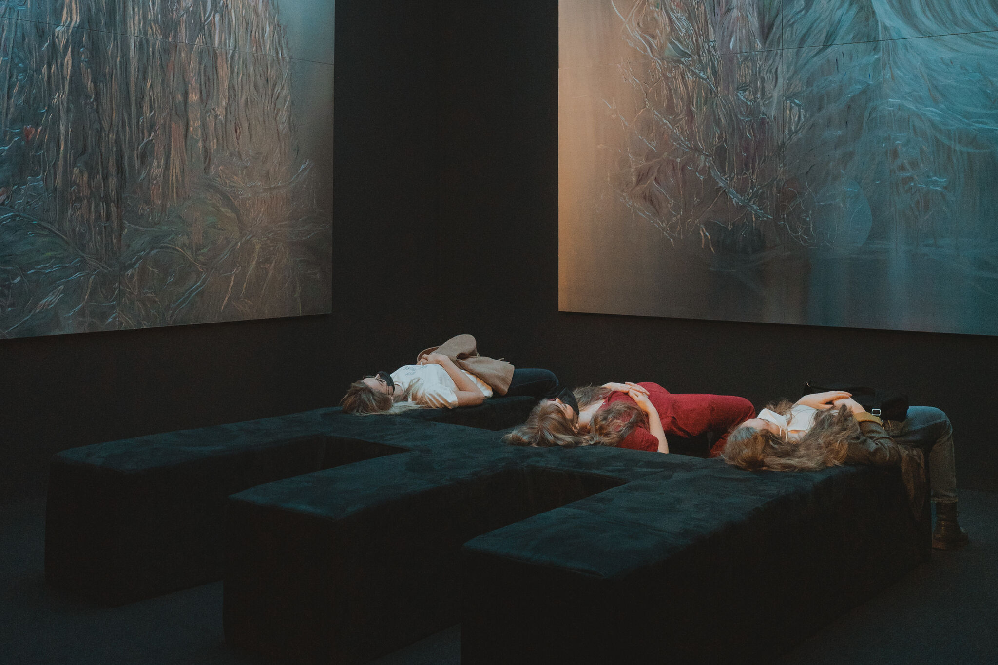 three people laying on a sofa looking at the ceiling in a gallery. 
