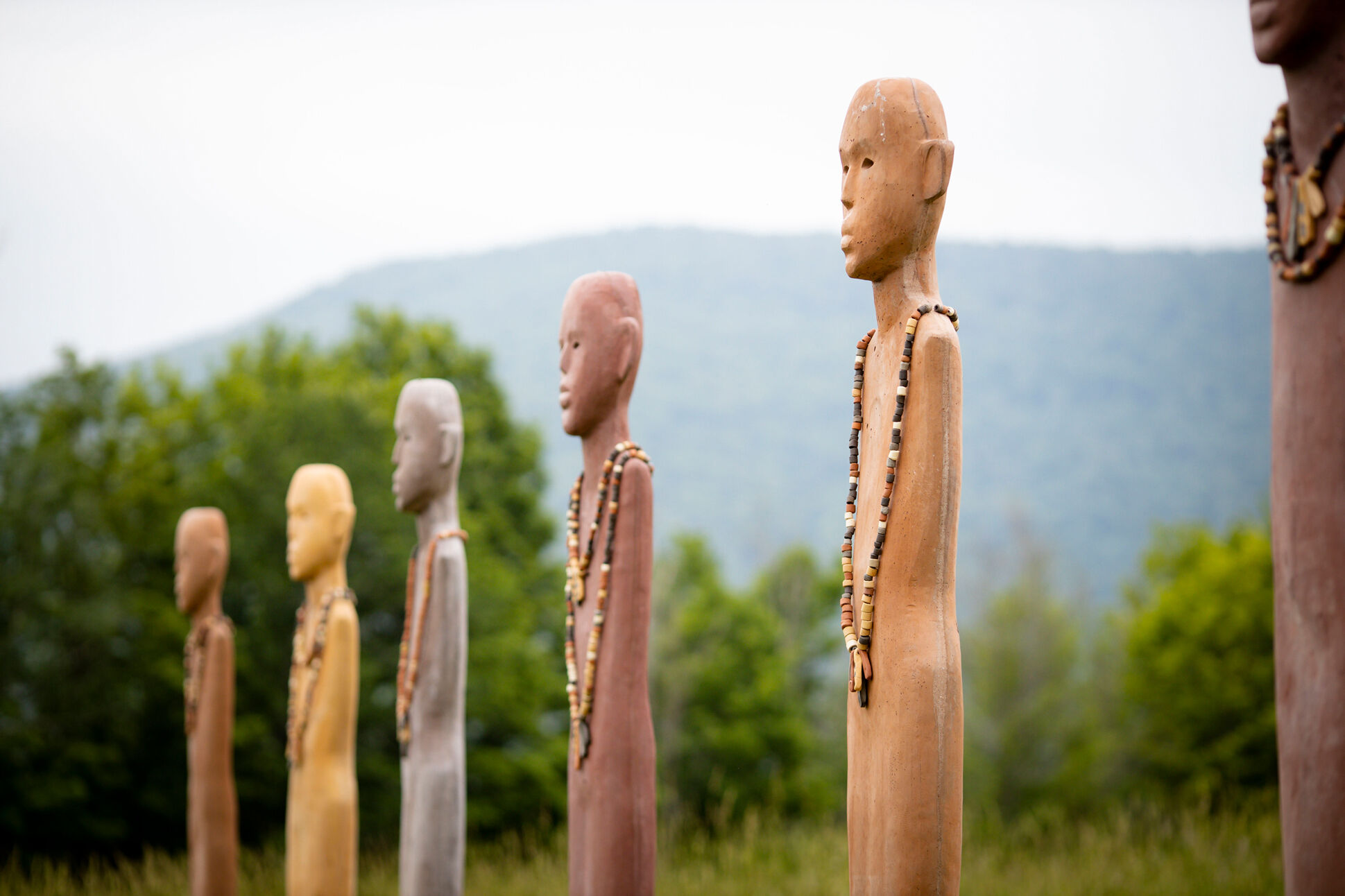 Figurative sculptures stand in a row against a blue sky with billowing clouds. 