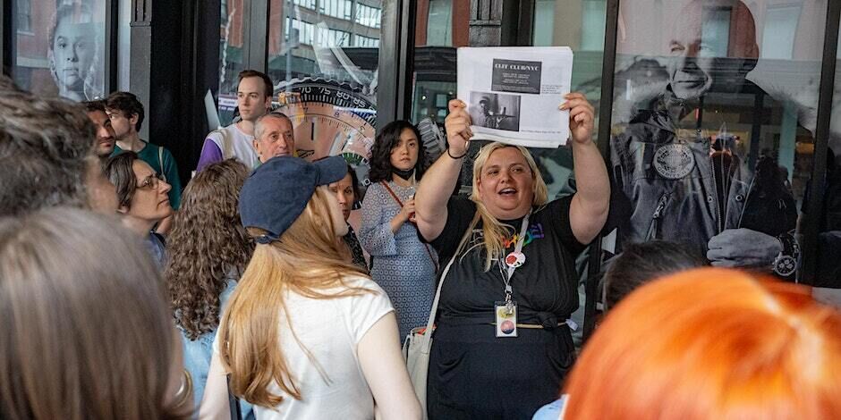 A person wearing a Whitney pride t-shirt holds up a piece of paper while giving a tour to participants.