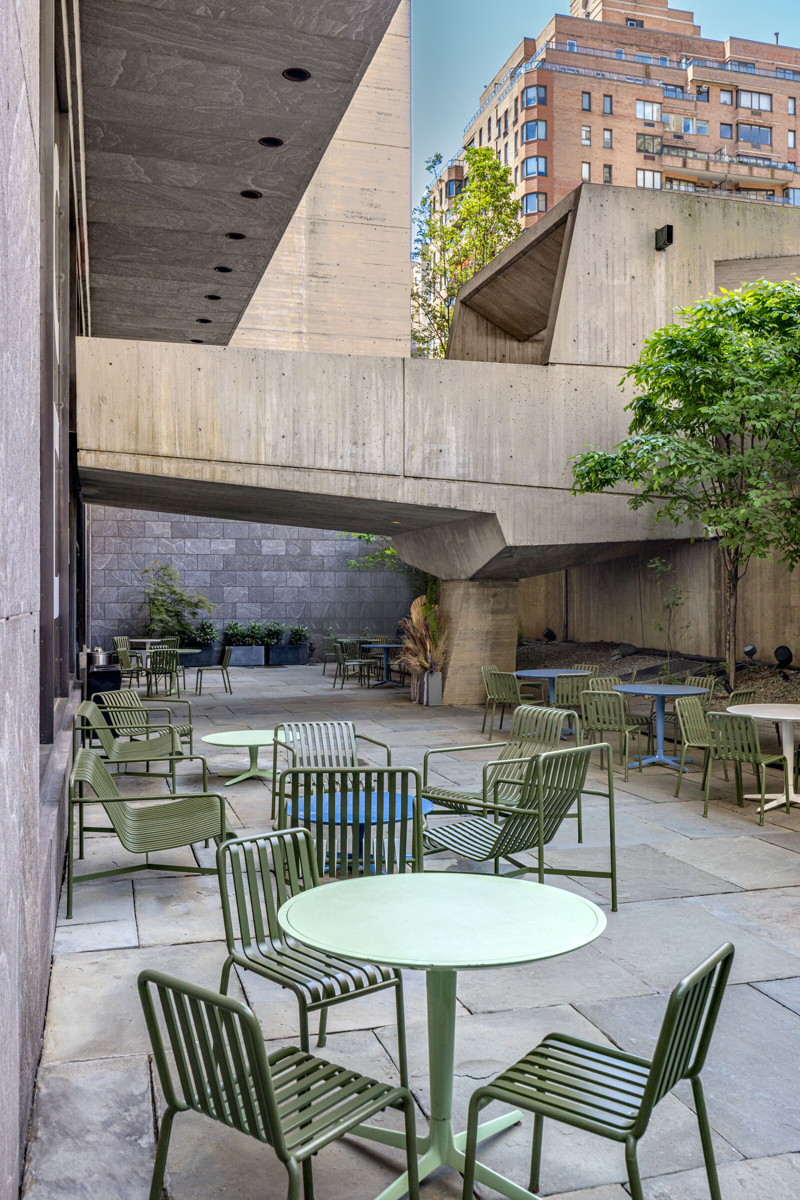 The outdoor terrace cafe at the Breuer Building with tables and leafy trees.