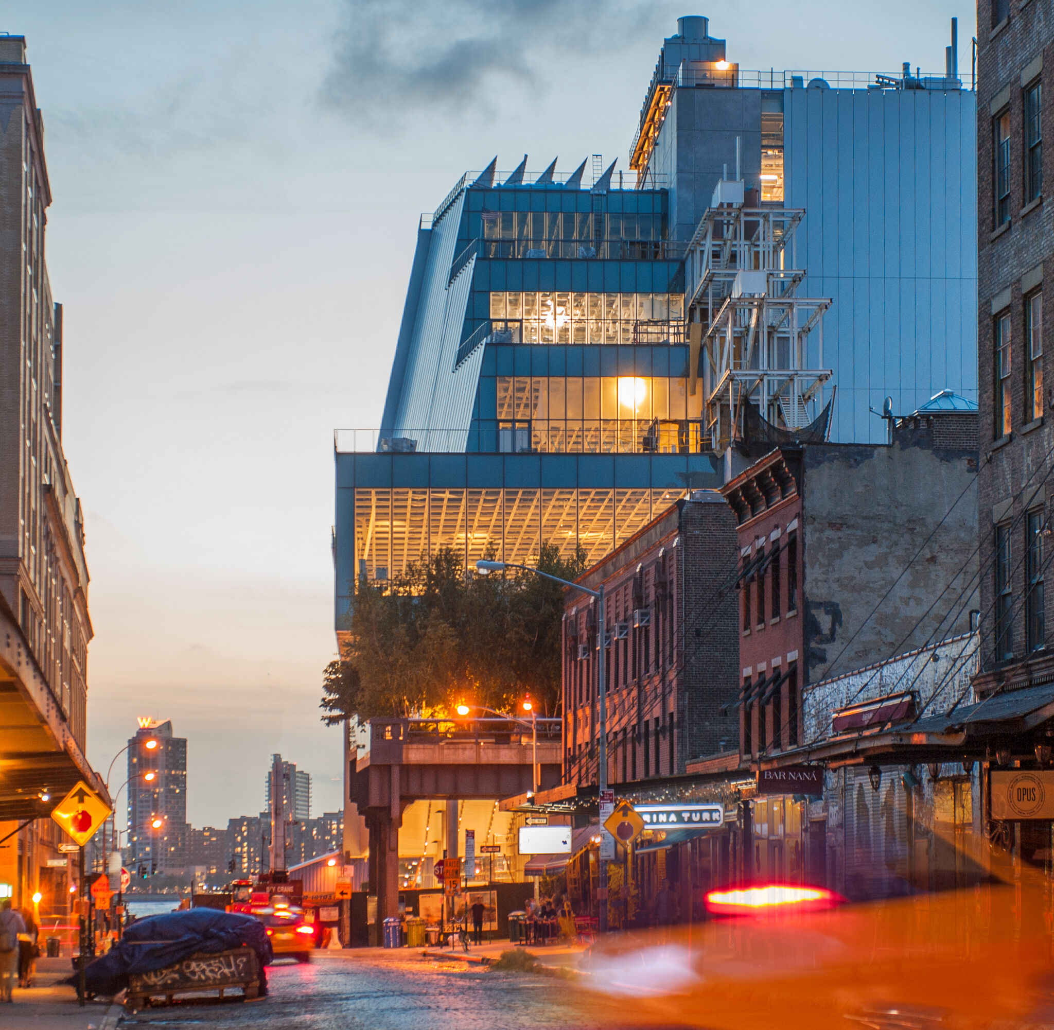 The Whitney Museum illuminated at night with the city skyline behind. 