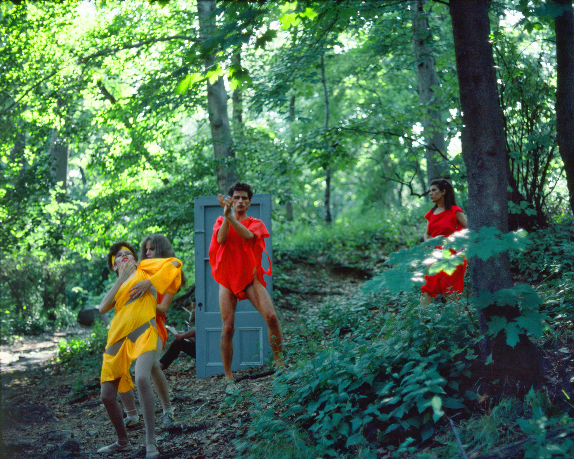 People in bright tunics move together in a forest. 