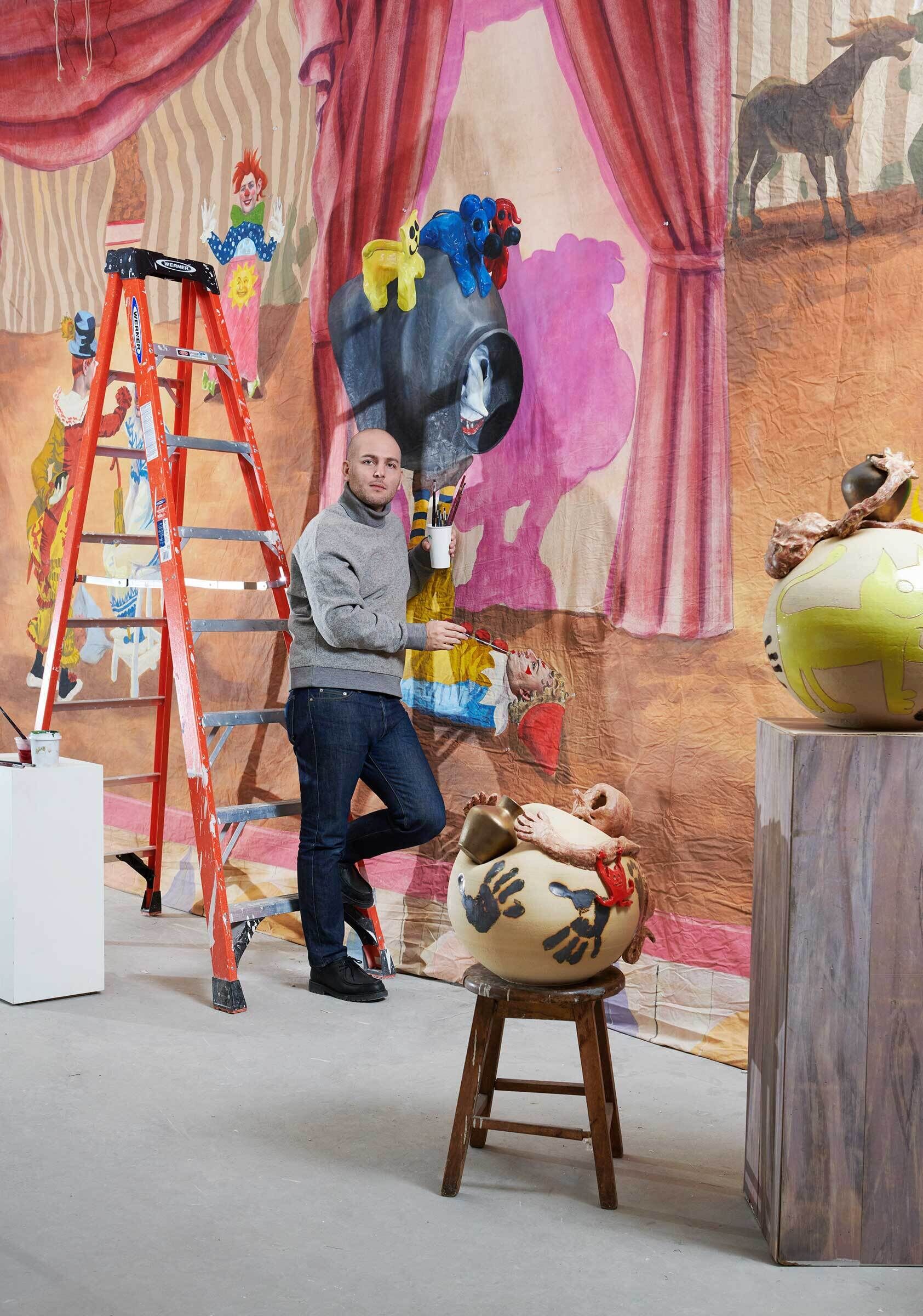 The artist Hadi Falapishi in his Brooklyn studio standing in front of his colorful works and a ladder.