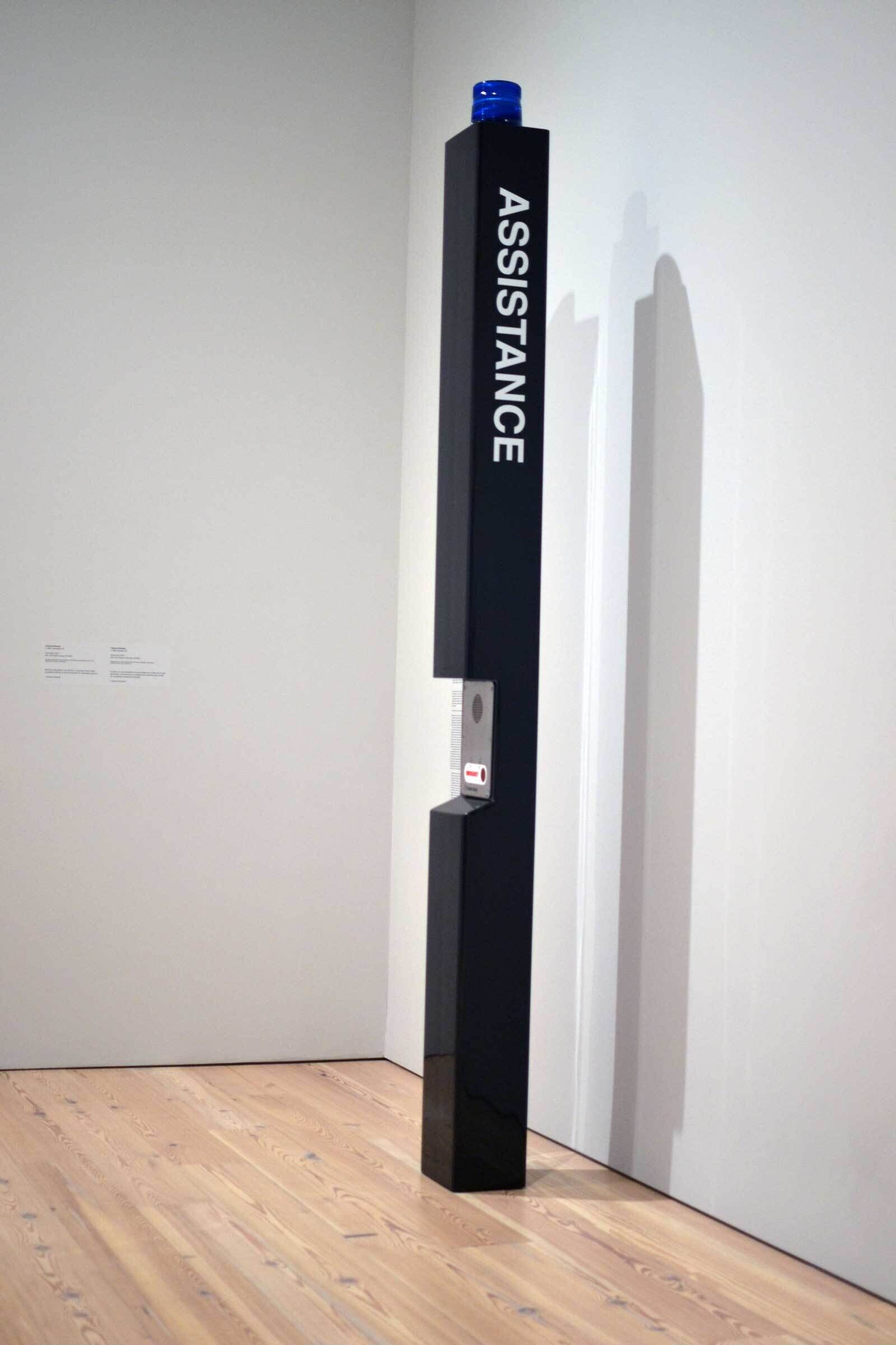A black pole with a blue light at the top and assistance written down along the side in white with an intercom system in the side.