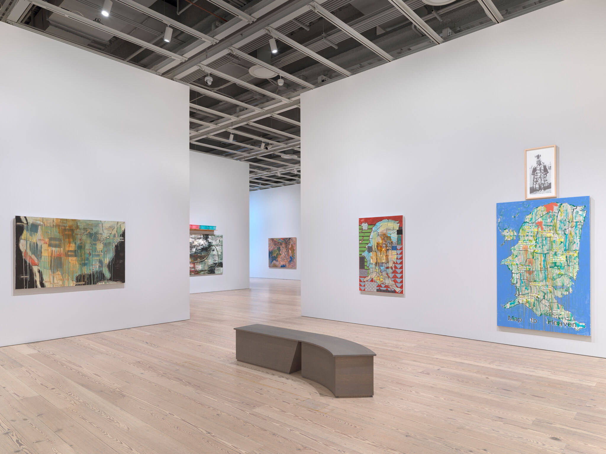 A view of a gallery with large paintings on the walls many of which depict maps. 