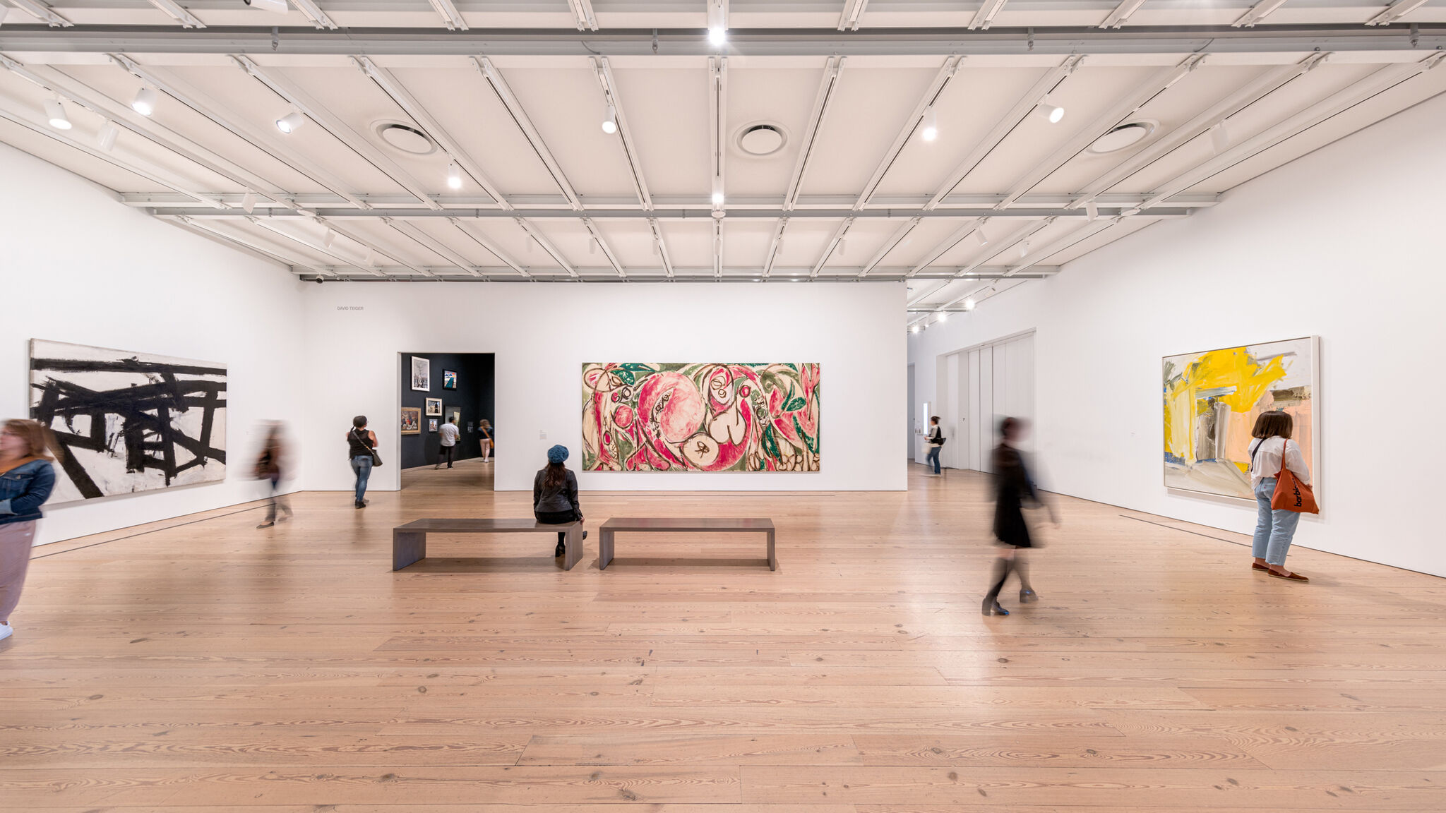 A large gallery with art on the walls. A large painting of organic pink and green shapes is at the center. 