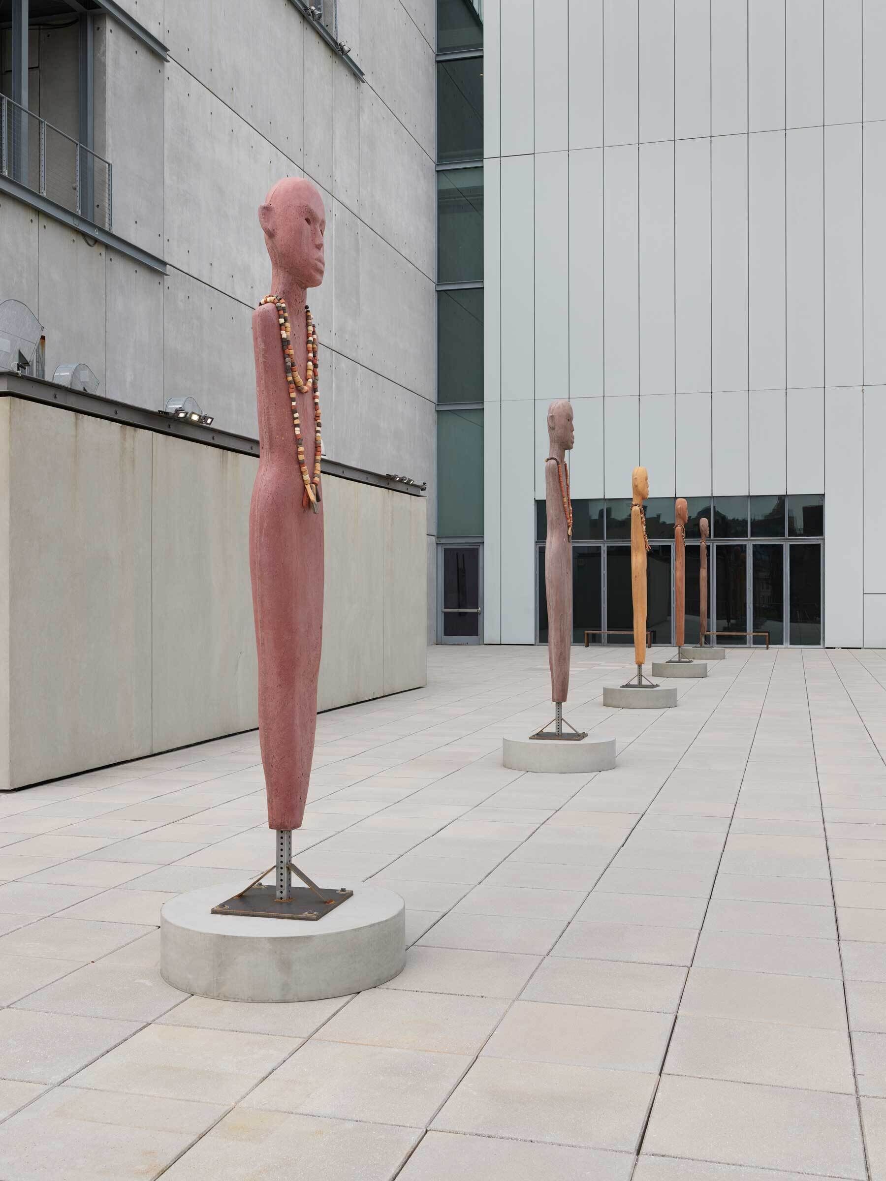 A profile view of tall human figure sculptures with no limbs stand straight on the balcony.