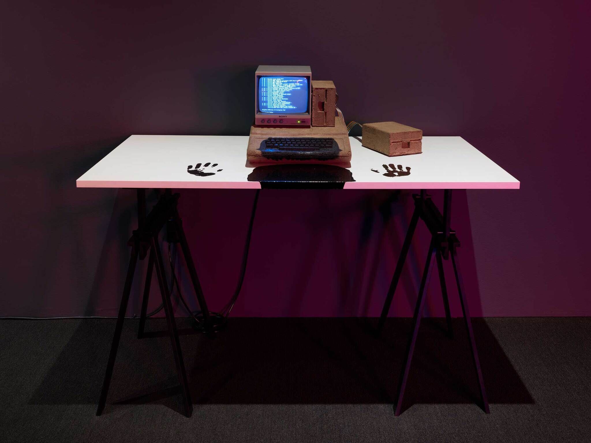 A white desk with a wooden computer and two dark handprints on either side.