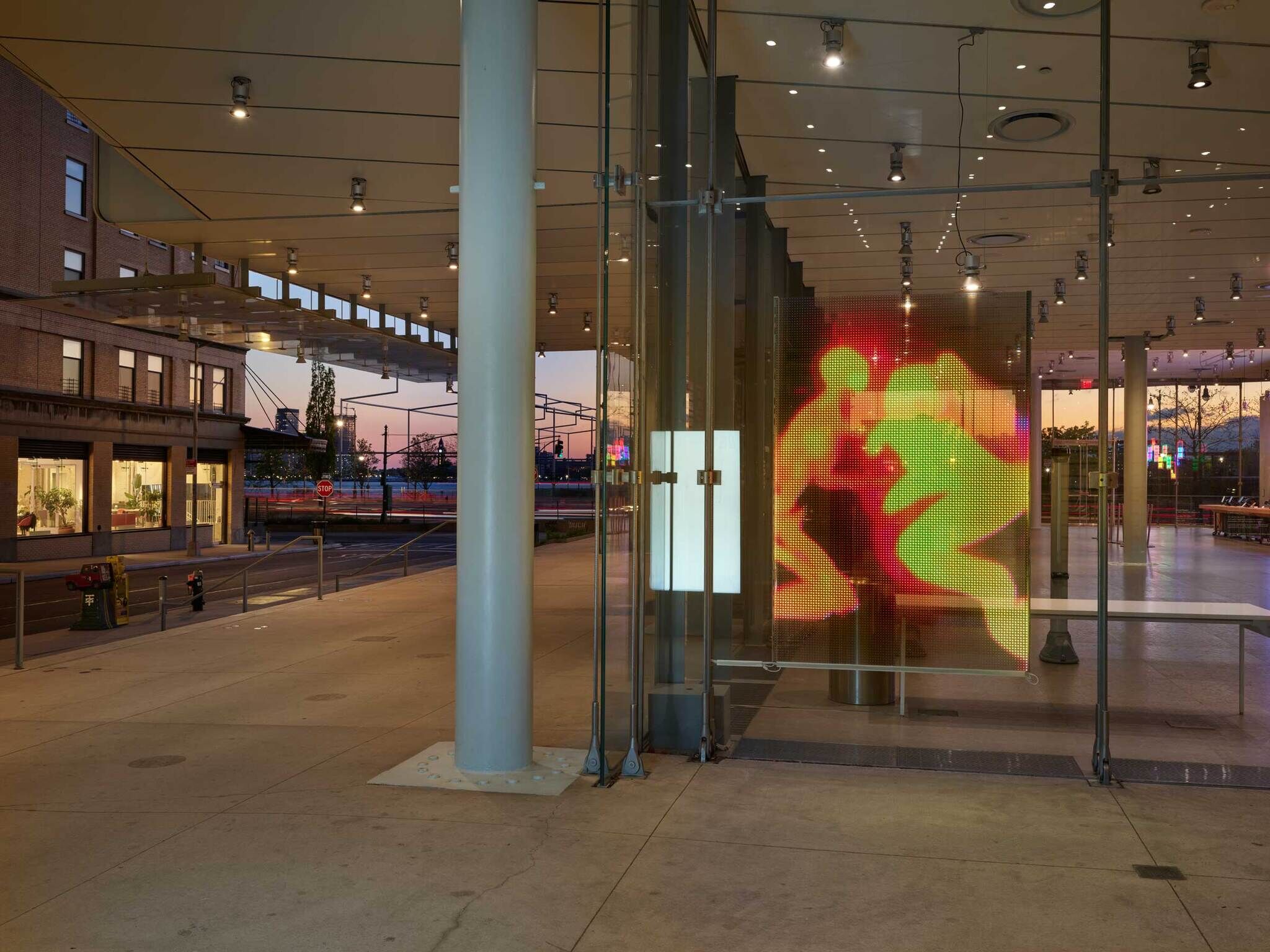 A projection of two red and yellow figures on the glass wall of the outside of the Whitney building.