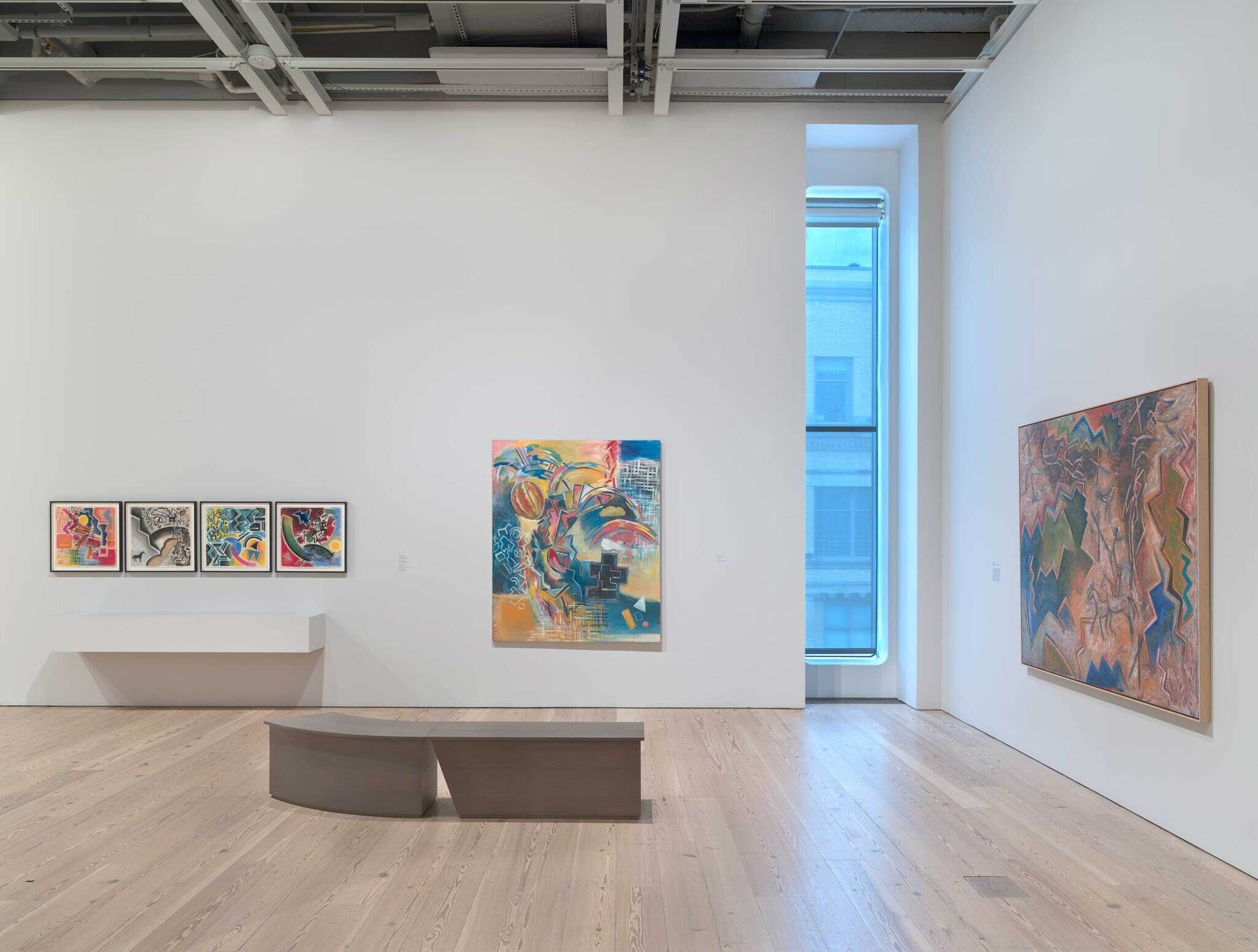 From left to right: four small color abstract paintings, a larger blue and yellow and pink abstract painting, and on the right, a landscape abstract painting.
