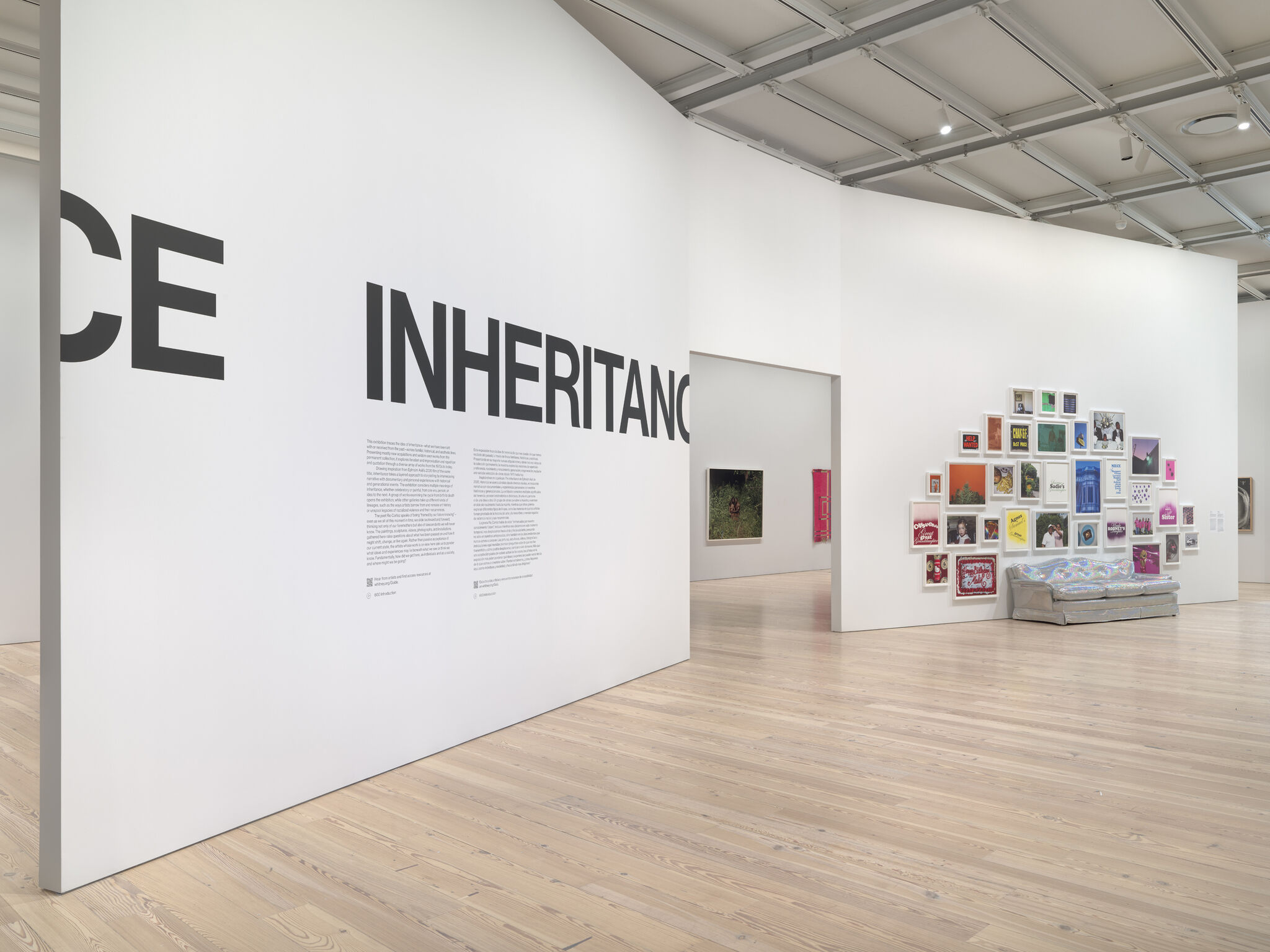 A wall with "Inheritance" in big letters with a smaller description text. To the right, an iridescent silver couch with a framed photographs above it in rainbow colors.