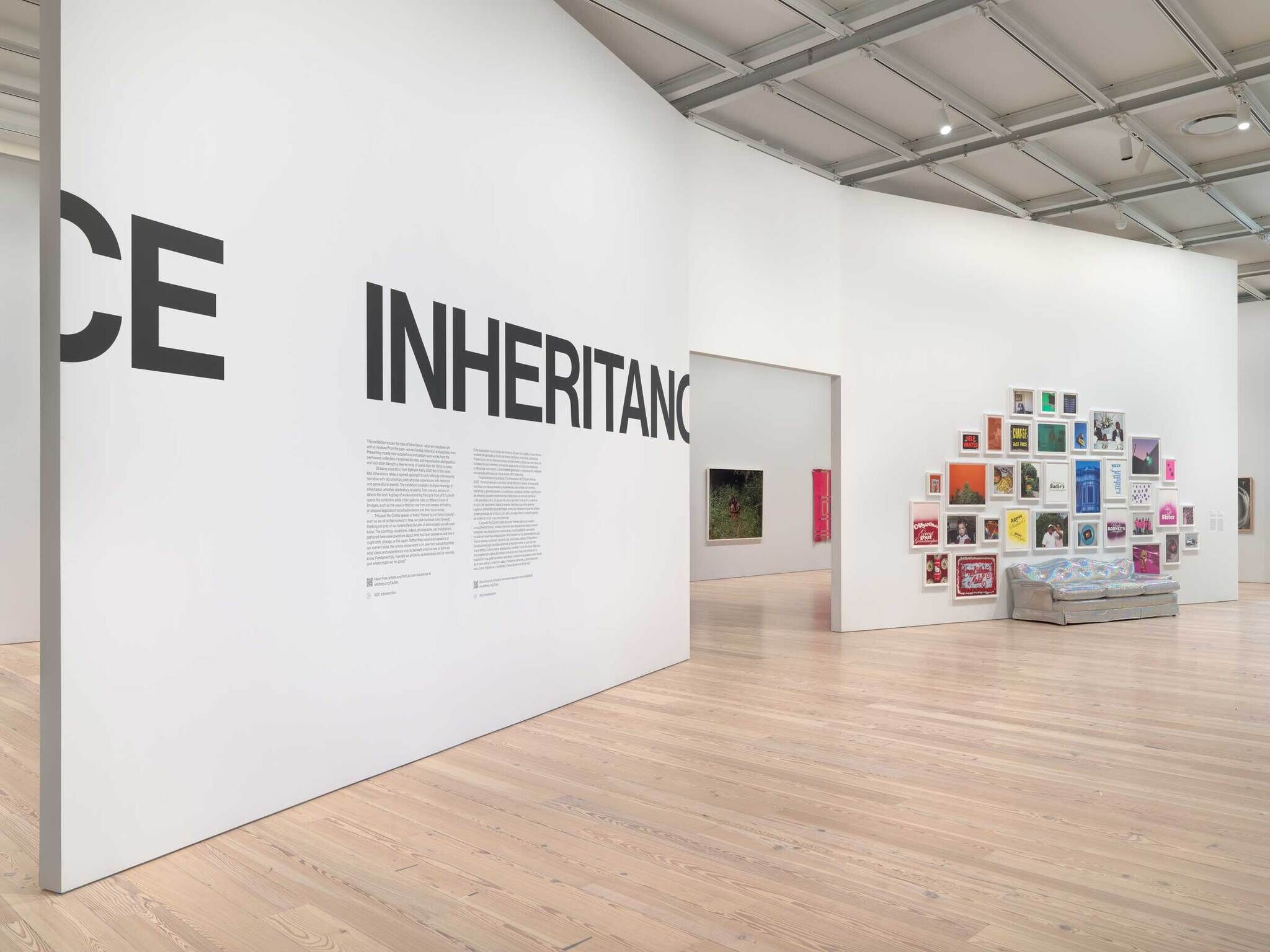 A wall with "Inheritance" in big letters with a smaller description text. To the right, an iridescent silver couch with a framed photographs above it in rainbow colors.