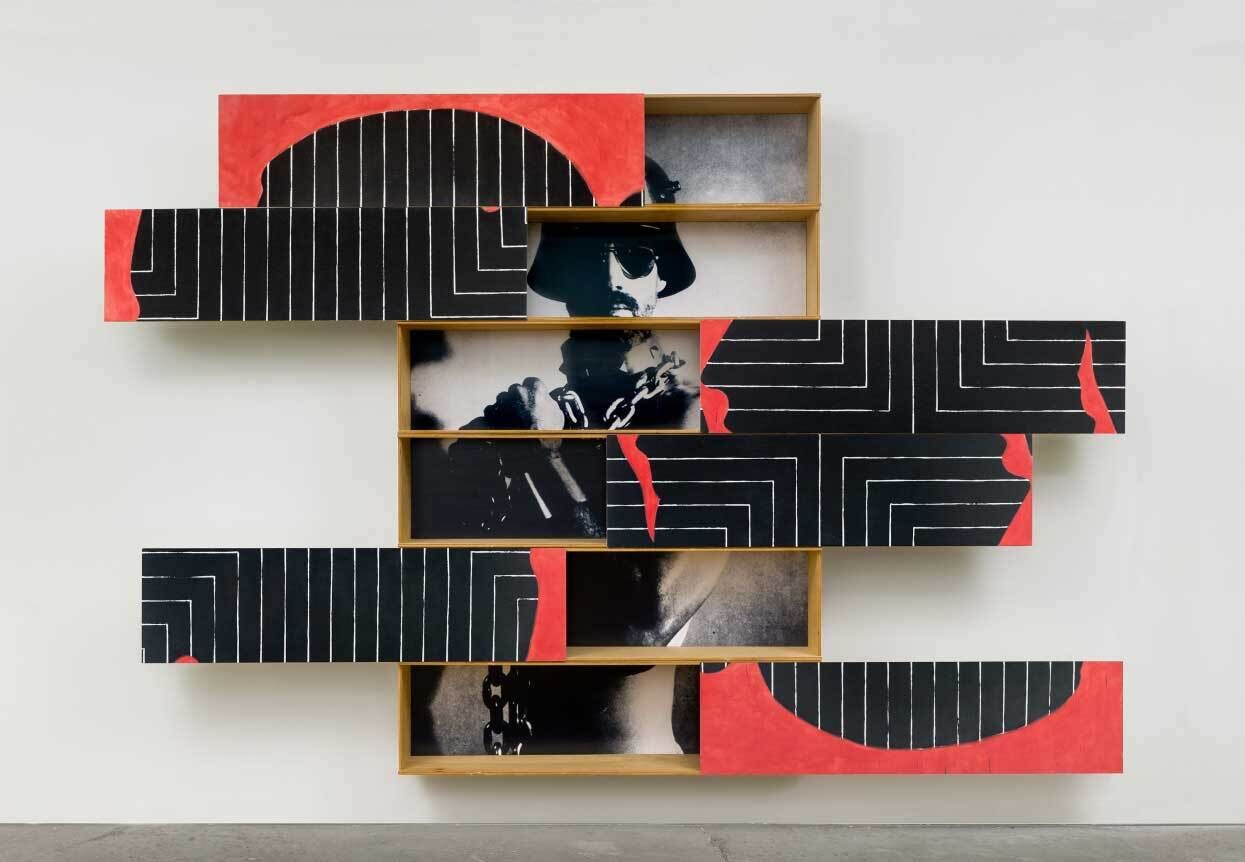 A photograph of a soldier in black and white behind shifting plywood pieces of red and black.